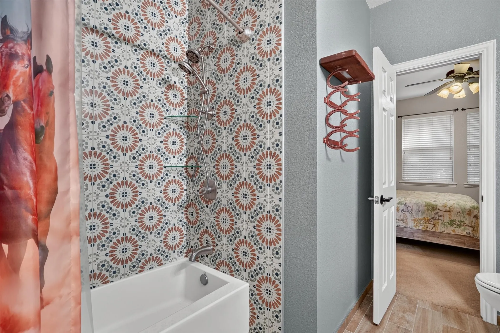 Bathtub with patterned tile surround, handheld shower fixture, and built-in glass shelving