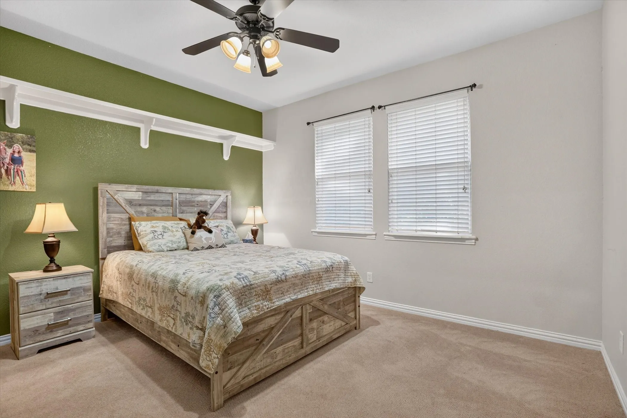 Ceiling fan with integrated lighting, wall-mounted shelving, twin windows with blinds, and neutral carpeting