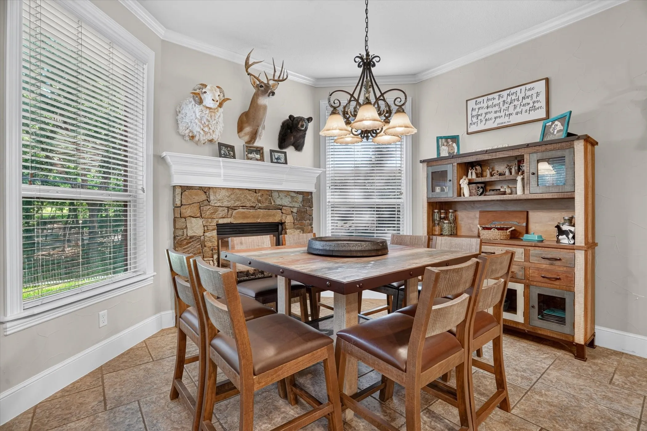 Stone-clad fireplace with a white mantel, crown molding, double windows, tiled flooring, and a decorative chandelier