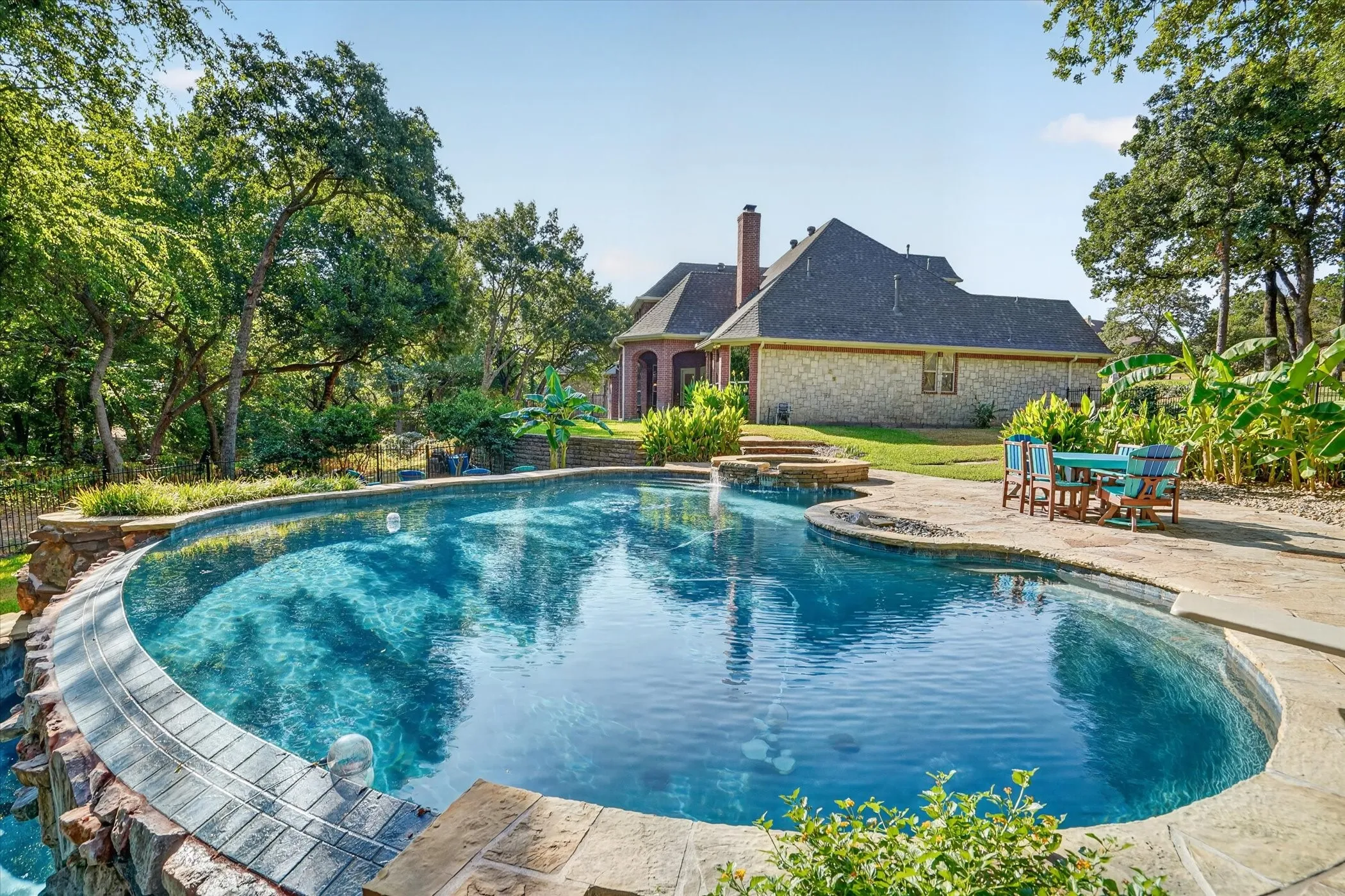 Curved infinity swimming pool with stone coping, a tiered waterfall feature, and surrounding stone patio