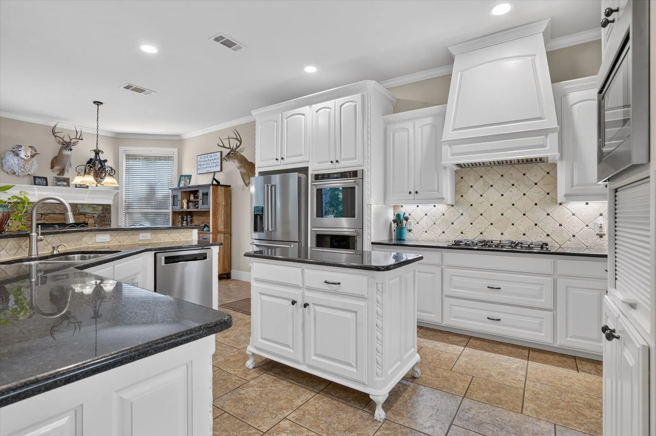 Ivory cabinetry, dark stone countertops, stainless steel appliances, tiled flooring, and a decorative range hood