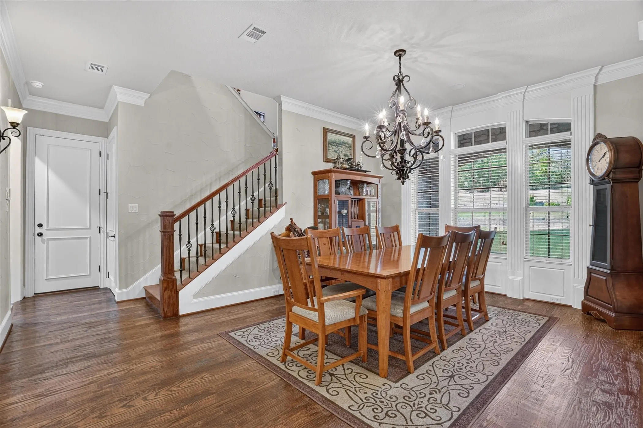 Hardwood-finish flooring, staircase with wood banister and wrought iron spindles, decorative chandelier, crown molding, and large windows with white trim wainscoting.