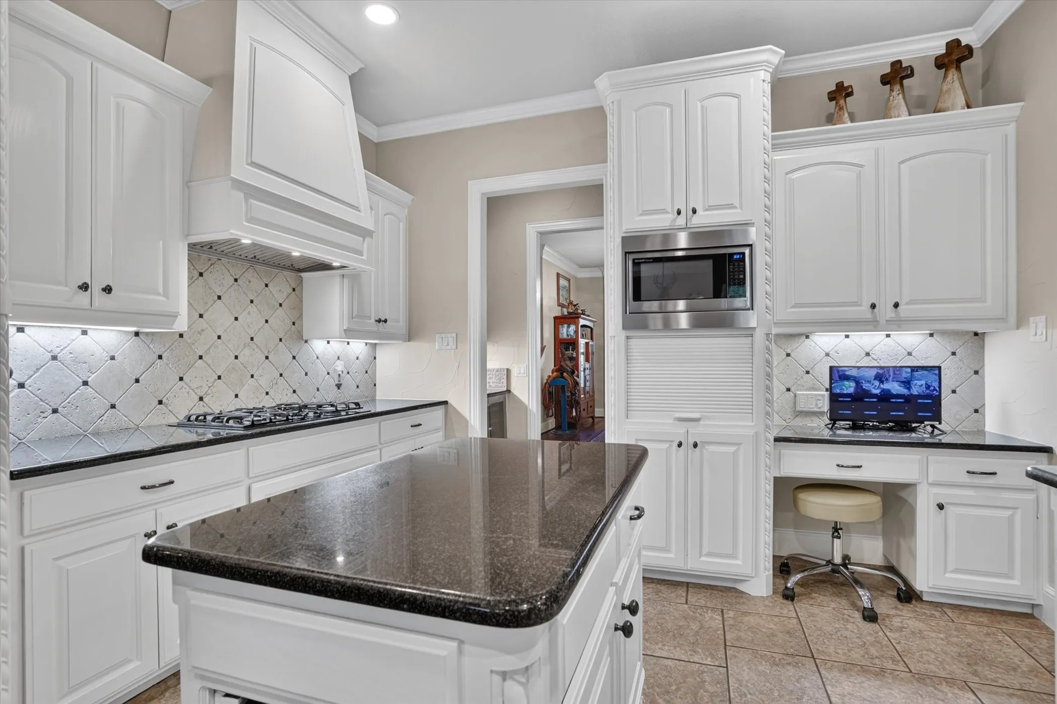 Ivory cabinetry, granite countertops, gas range with custom hood, diagonal tile backsplash, and stainless steel built-in microwave