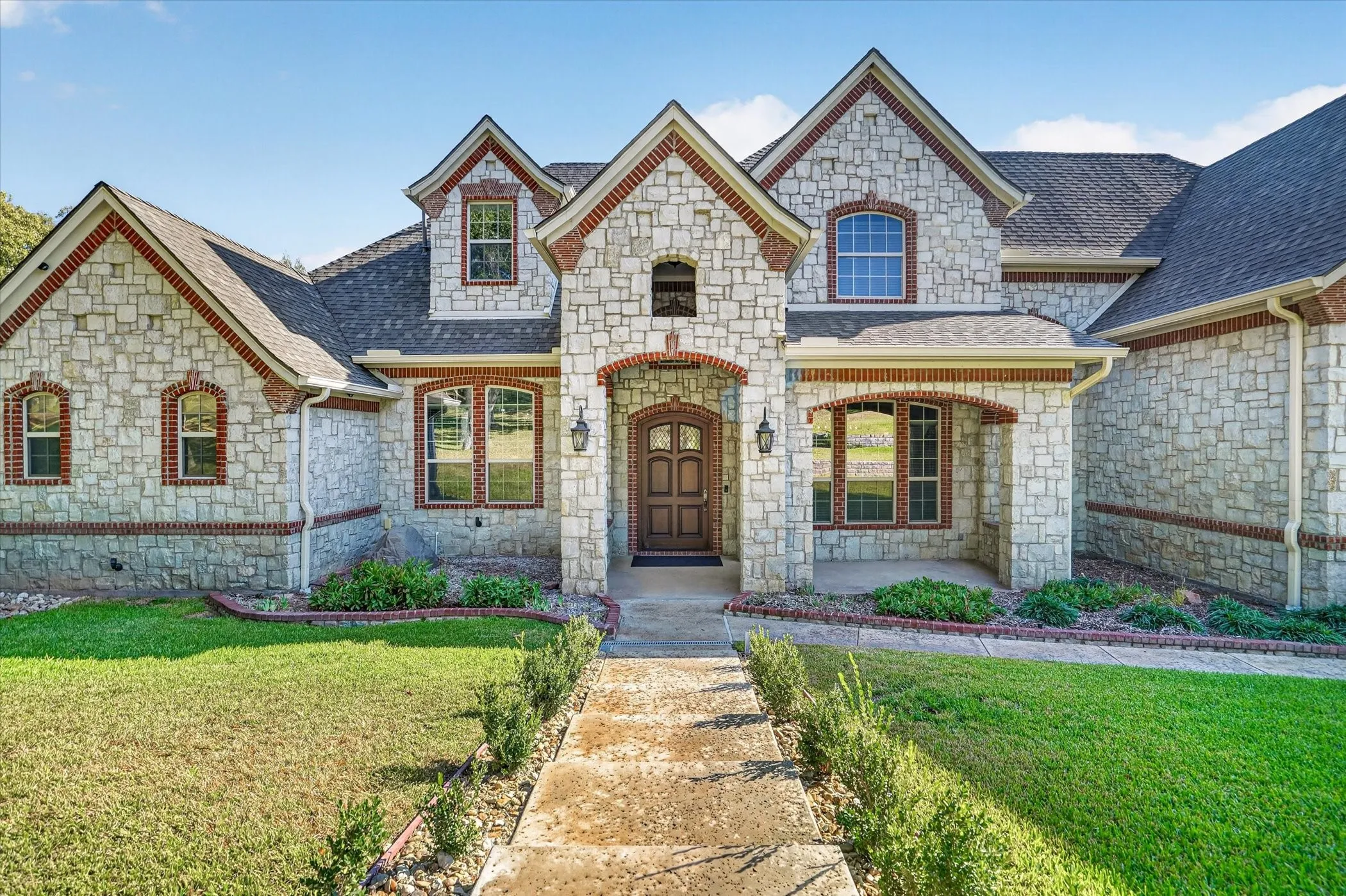 Stone and brick exterior with arched window accents, a covered front entry, and a paved walkway