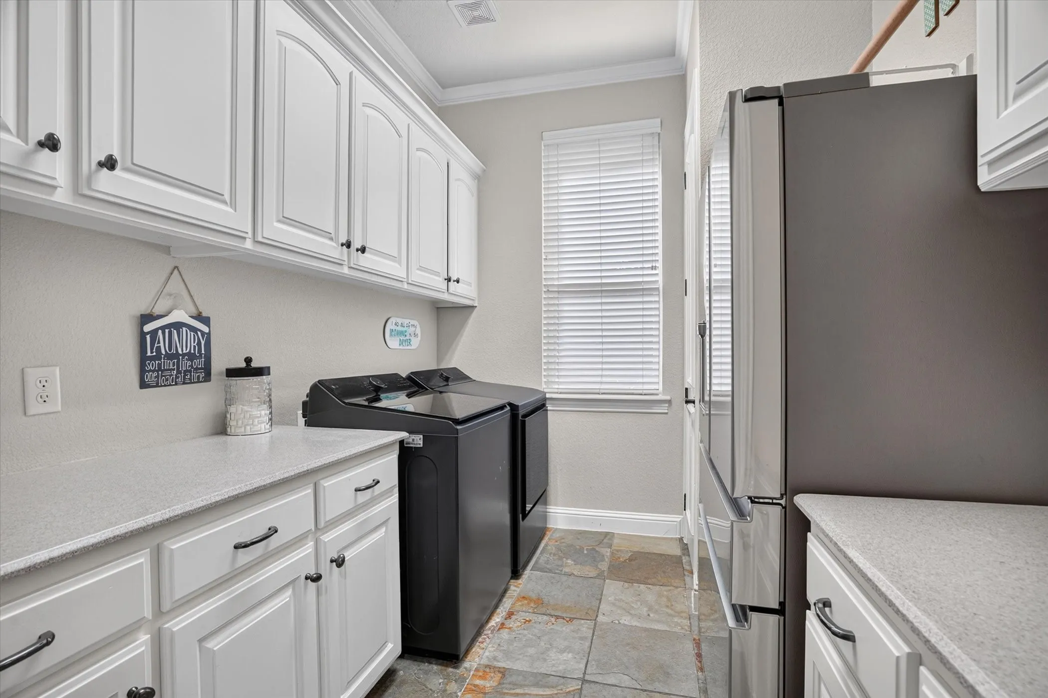 Ivory cabinetry with dark hardware, light countertops, and slate tile flooring