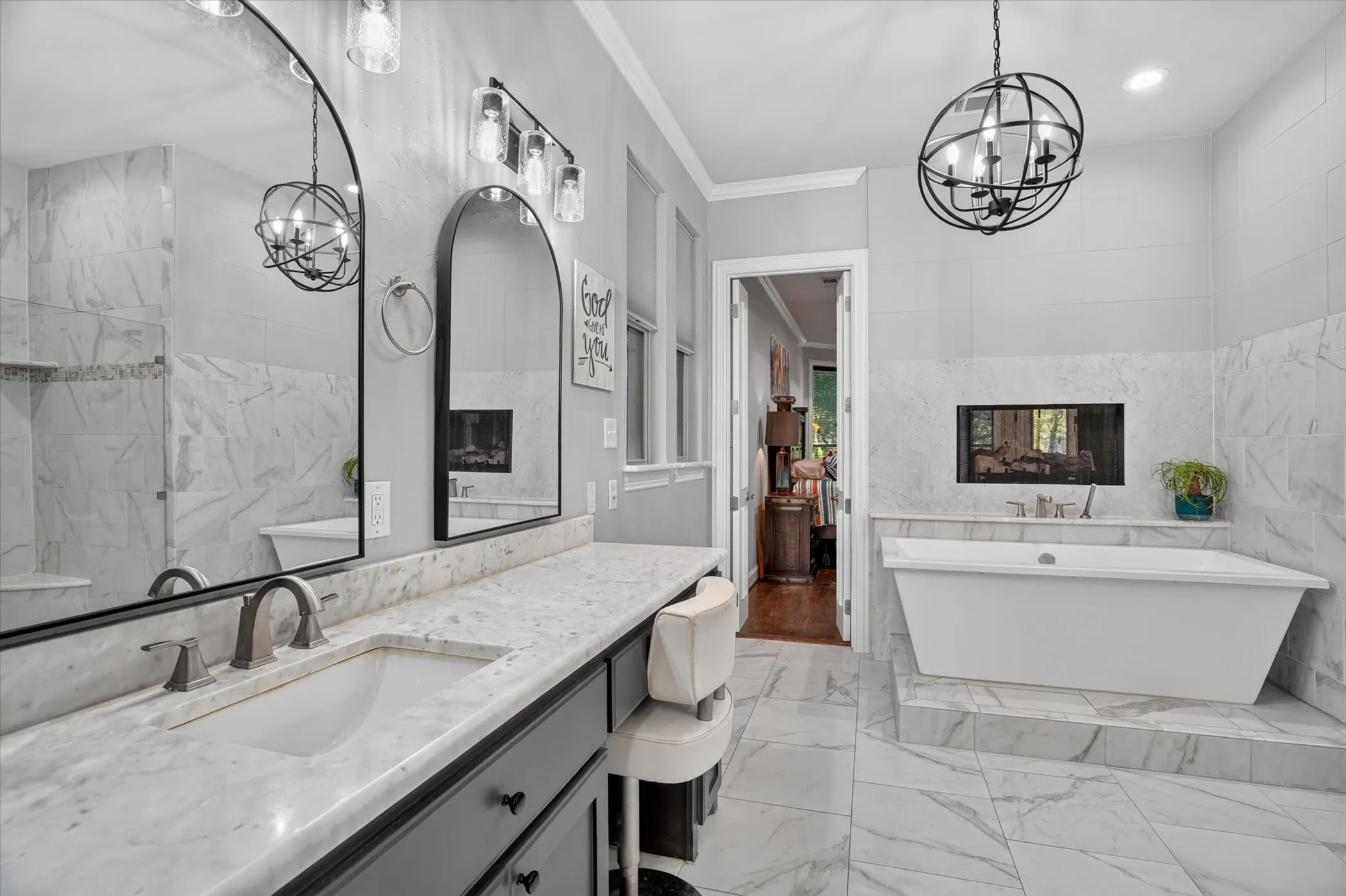 Freestanding soaking tub with a built-in fireplace, marble-look tiled floor, dual vanities and contemporary light fixtures