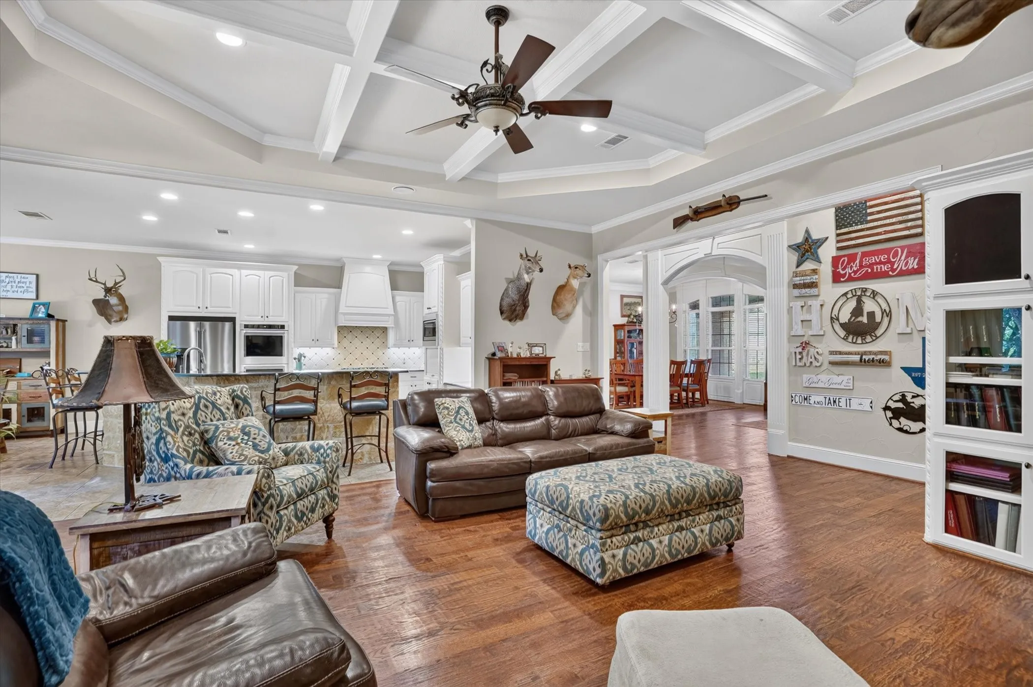 Tray ceiling with decorative beams, wood-finish flooring, recessed lighting, arched doorways, and built-in cabinetry