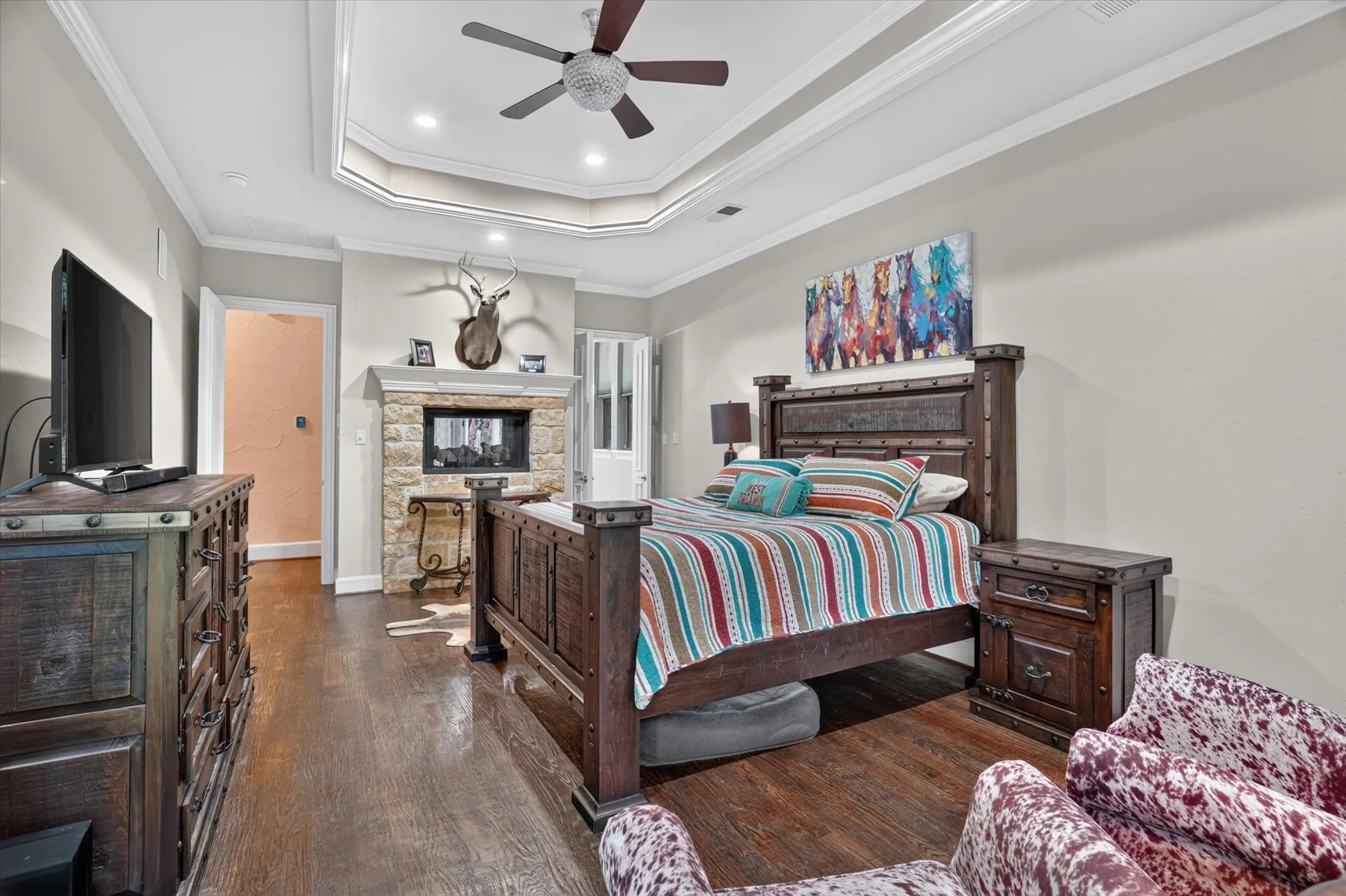 Tray ceiling with recessed lighting and a ceiling fan, stone fireplace with a mantel, and dark wood flooring