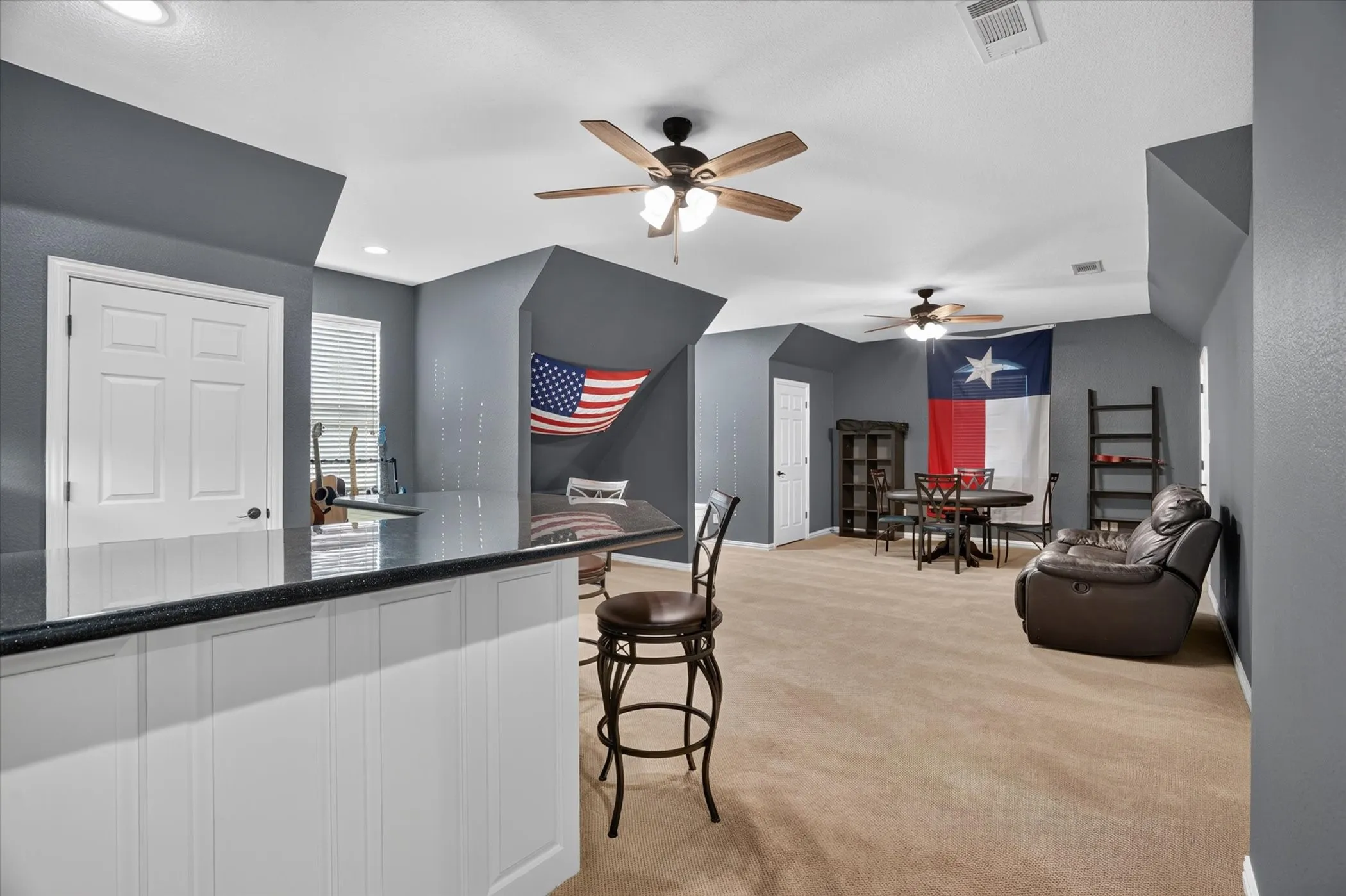 Built-in bar with dark countertop and paneling, two ceiling fans, carpeted flooring, and a white paneled door