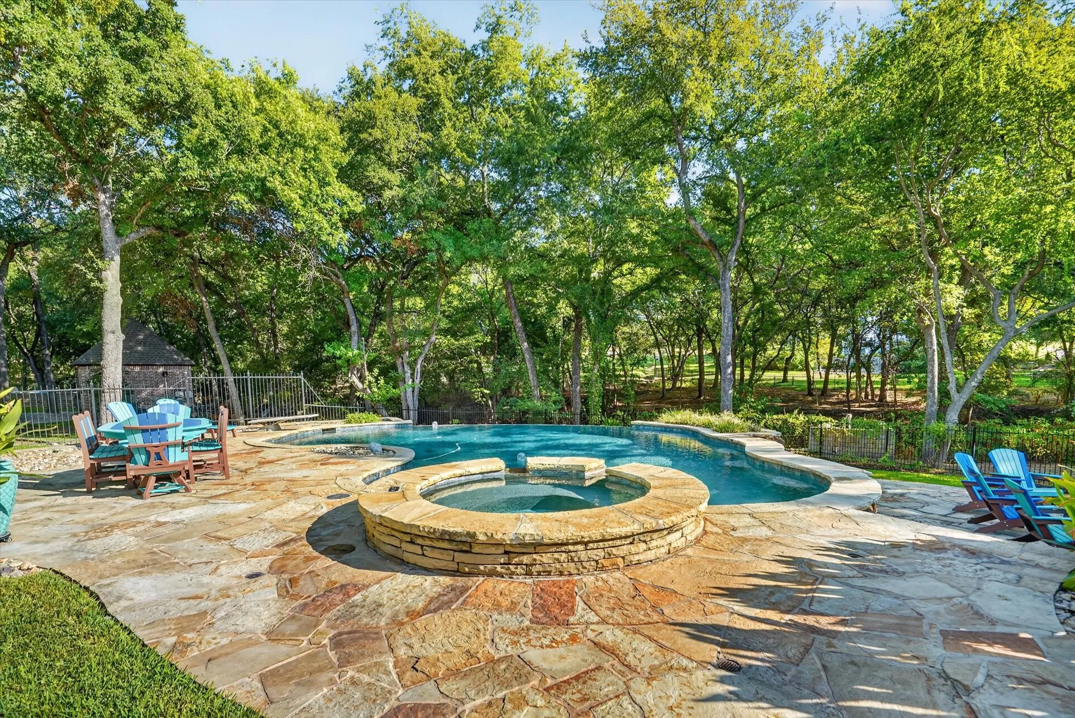 Curved Infinity swimming pool with integrated spa, surrounded by a flagstone patio and mature trees