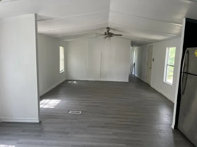 Vaulted ceiling with a ceiling fan, grey wood-finish flooring, and white walls