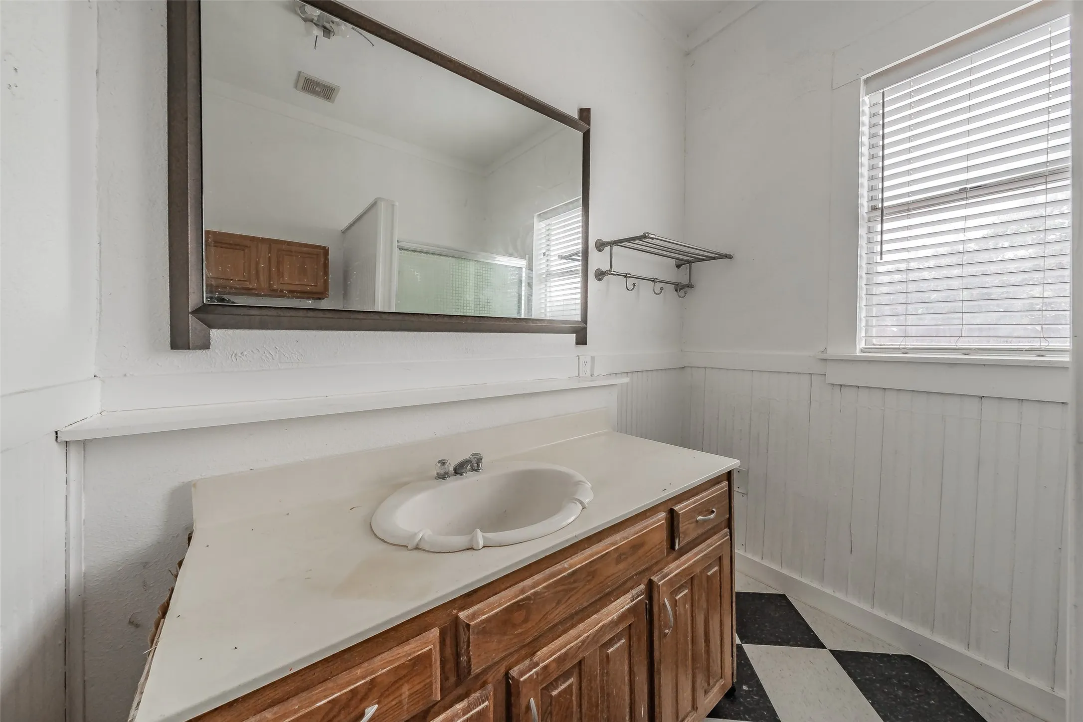 Wood-finish vanity with an integrated sink, large wall mirror, and a window with horizontal blinds