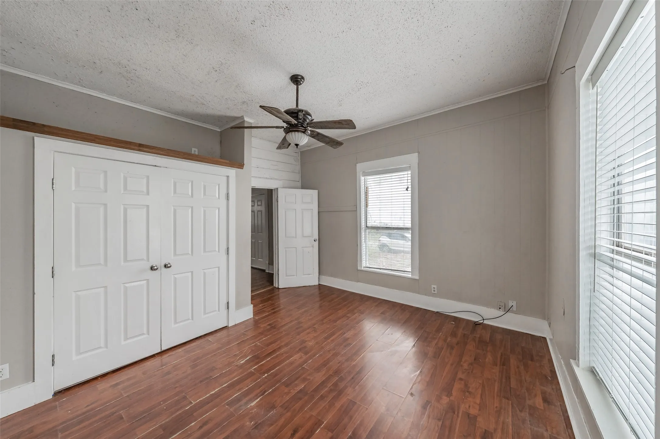 Wood-finish flooring, white panel doors, a ceiling fan with light fixture, and multiple windows with blinds