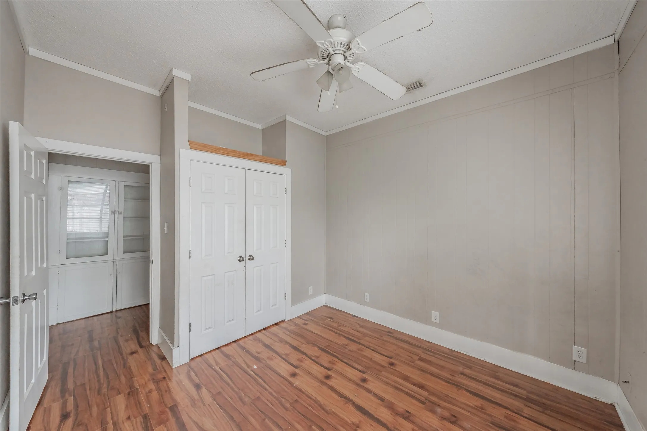 Hardwood-finish flooring throughout, white ceiling fan, crown molding, white paneled doors, and built-in cabinetry with glass panels