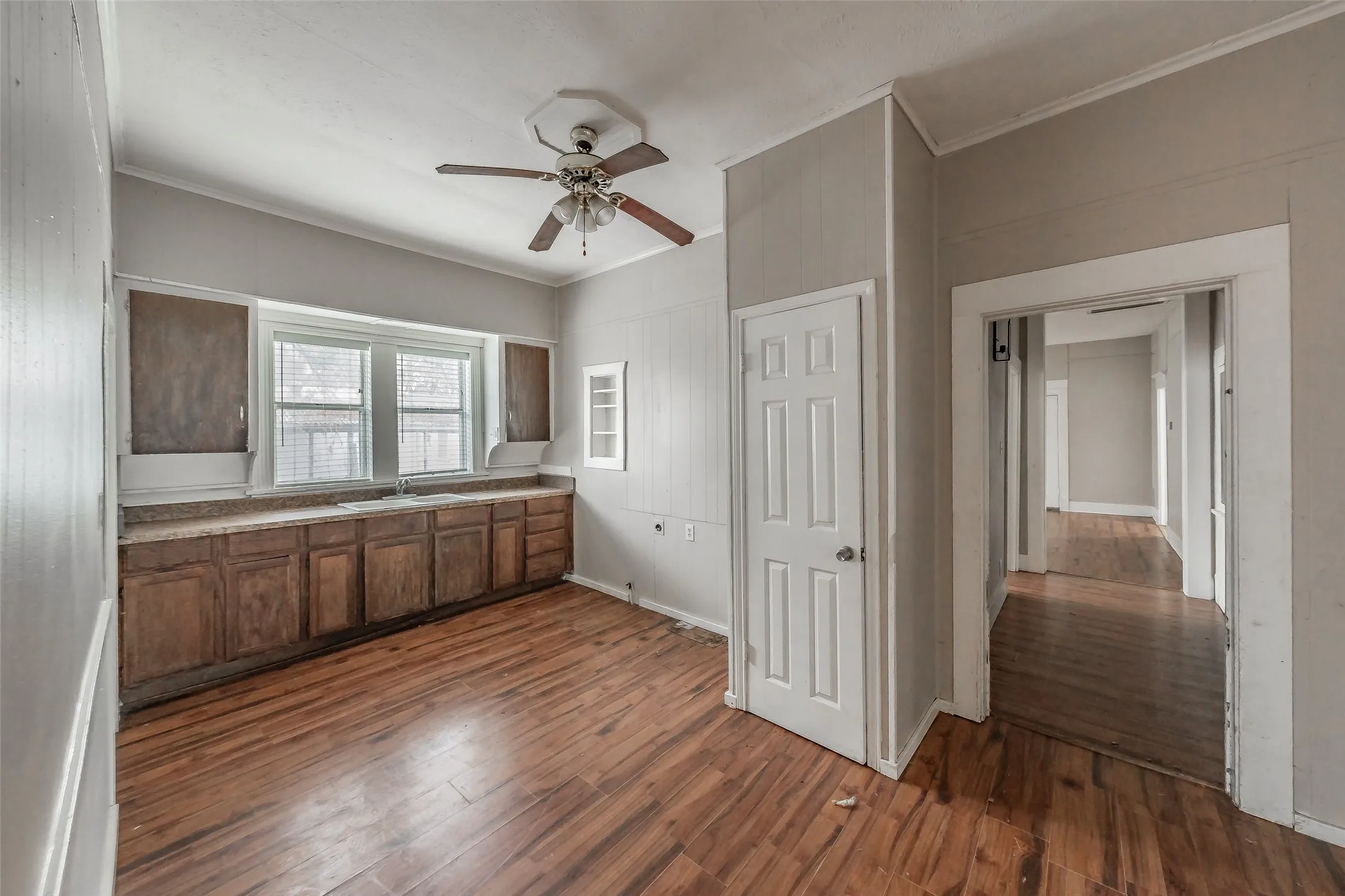Wood-finish flooring, built-in cabinetry, two windows with blinds, ceiling fan with light fixture, and a paneled interior door