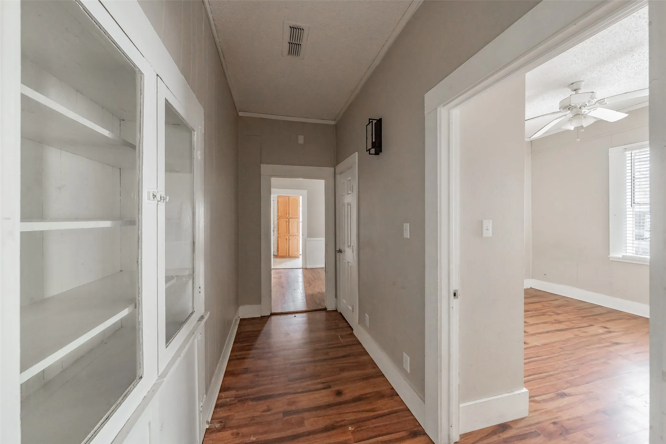Wood-finish flooring throughout, built-in display cabinet with glass doors, and a ceiling fan with light kit