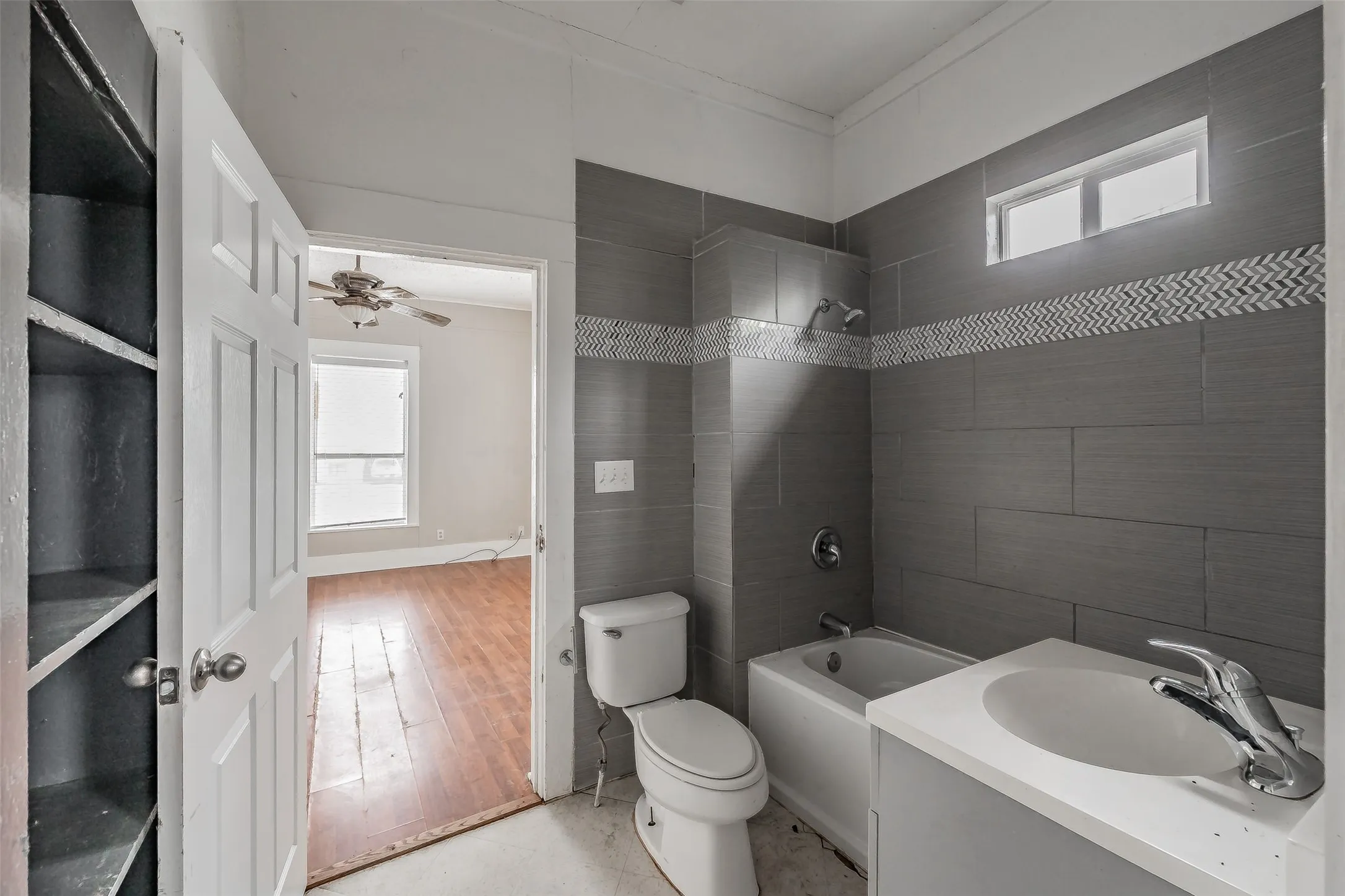 Bathroom featuring a tiled shower surround with decorative accent, single vanity, and built-in shelving