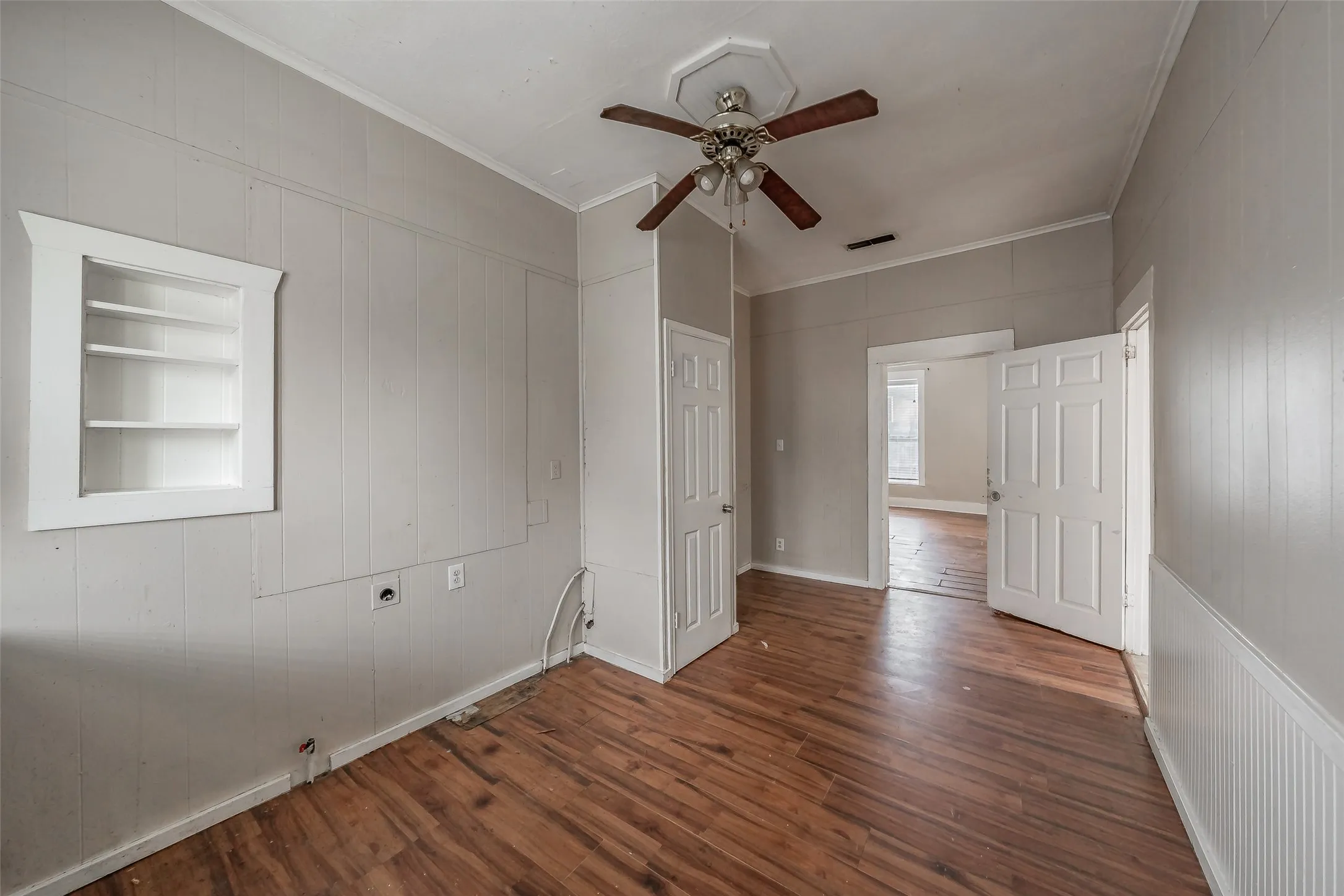 Wood-finish flooring, built-in shelving, paneled walls, and a ceiling fan with light fixture