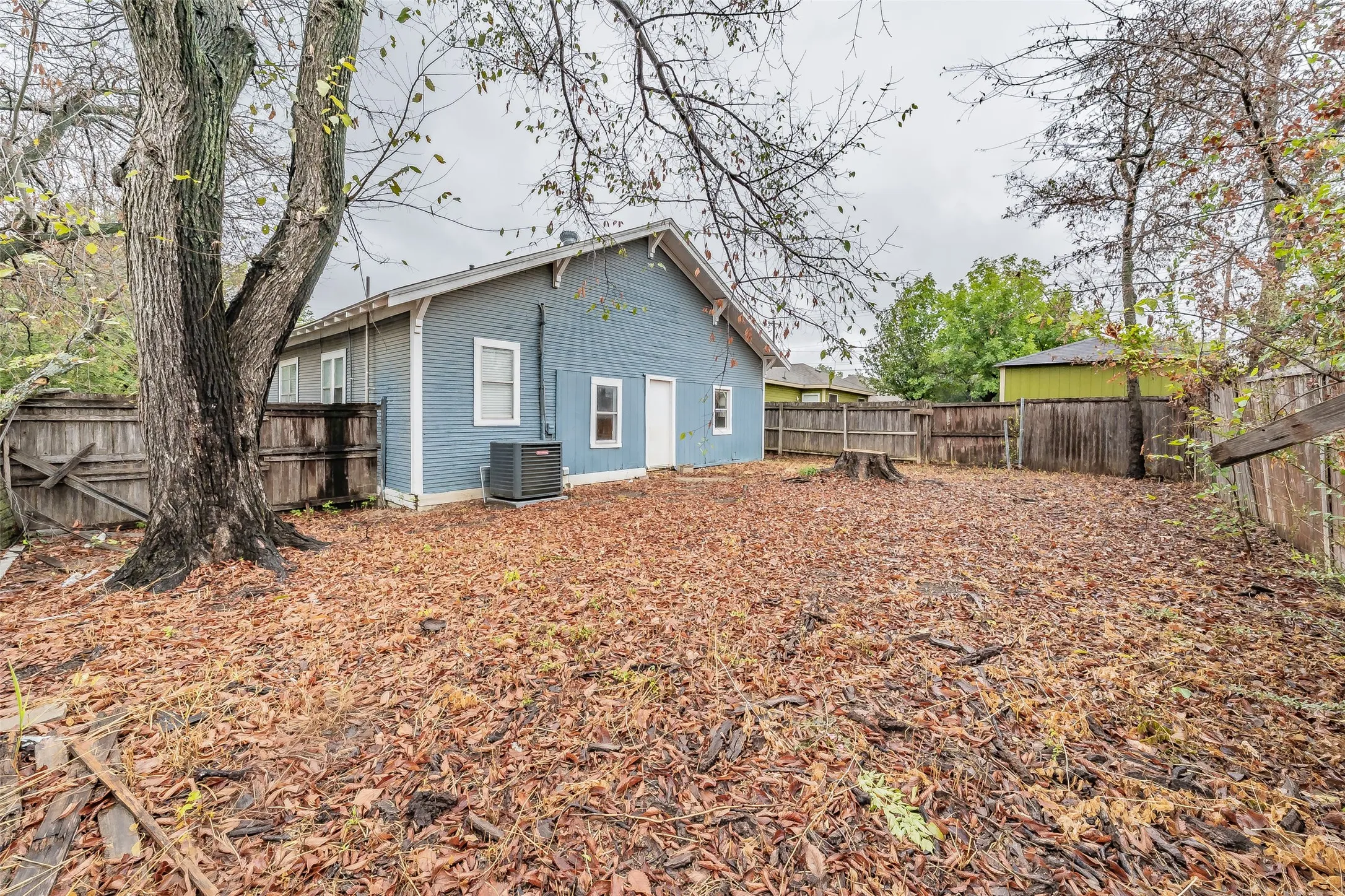 Blue siding exterior, multiple windows, external HVAC unit, wood fencing, mature trees