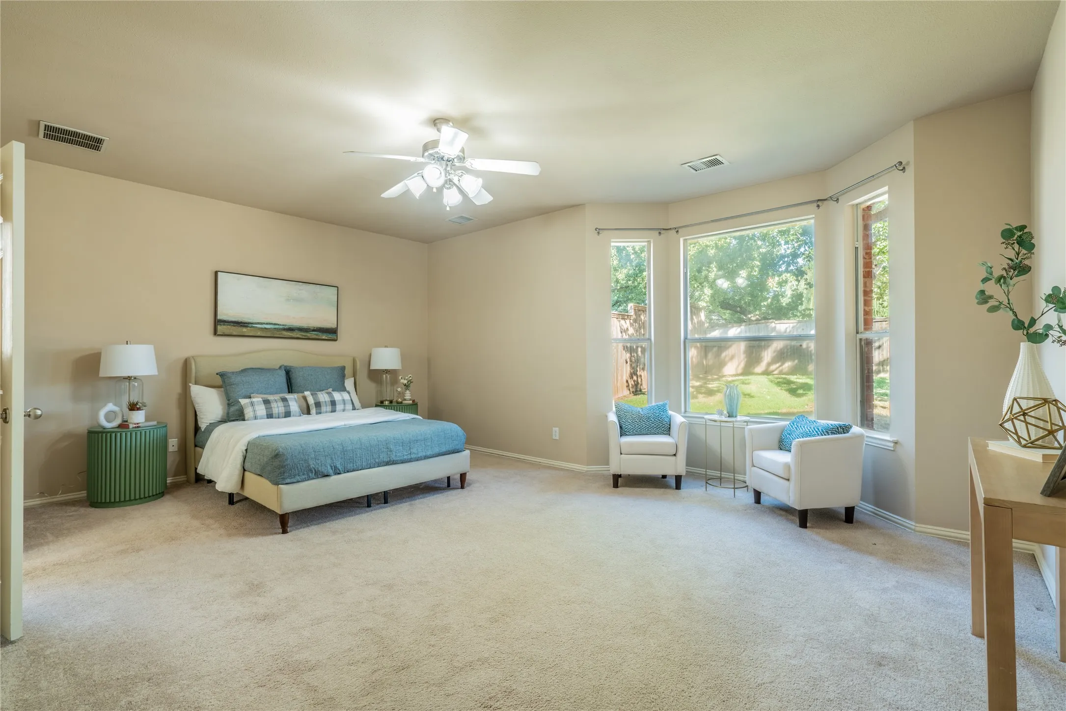 Expansive primary bedroom featuring carpeted flooring, a ceiling fan, and a prominent bay window