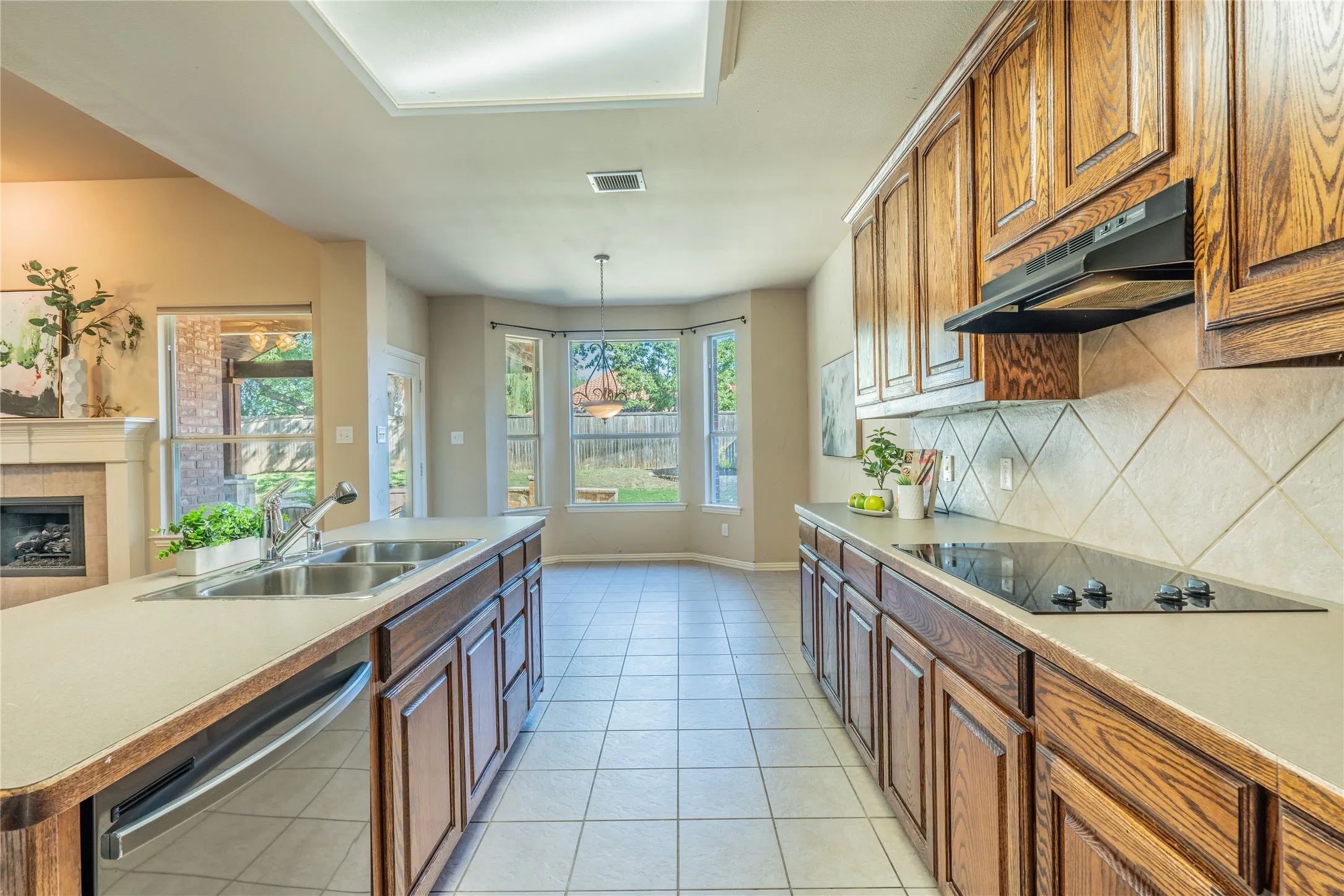Kitchen featuring tile flooring, wooden cabinetry, an electric cooktop, a double basin sink, and a tiled backsplash