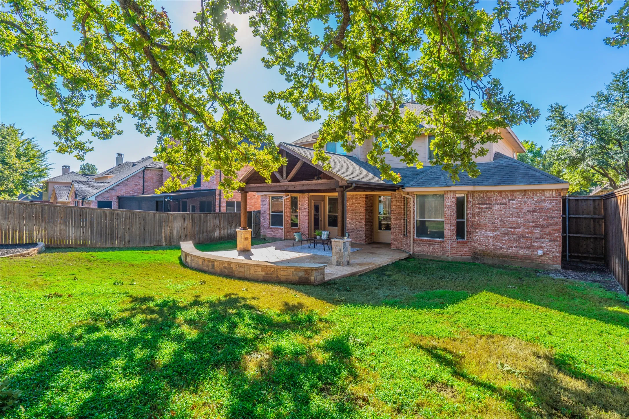 Manicured backyard featuring a covered patio, extensive hardscaping, and privacy fencing