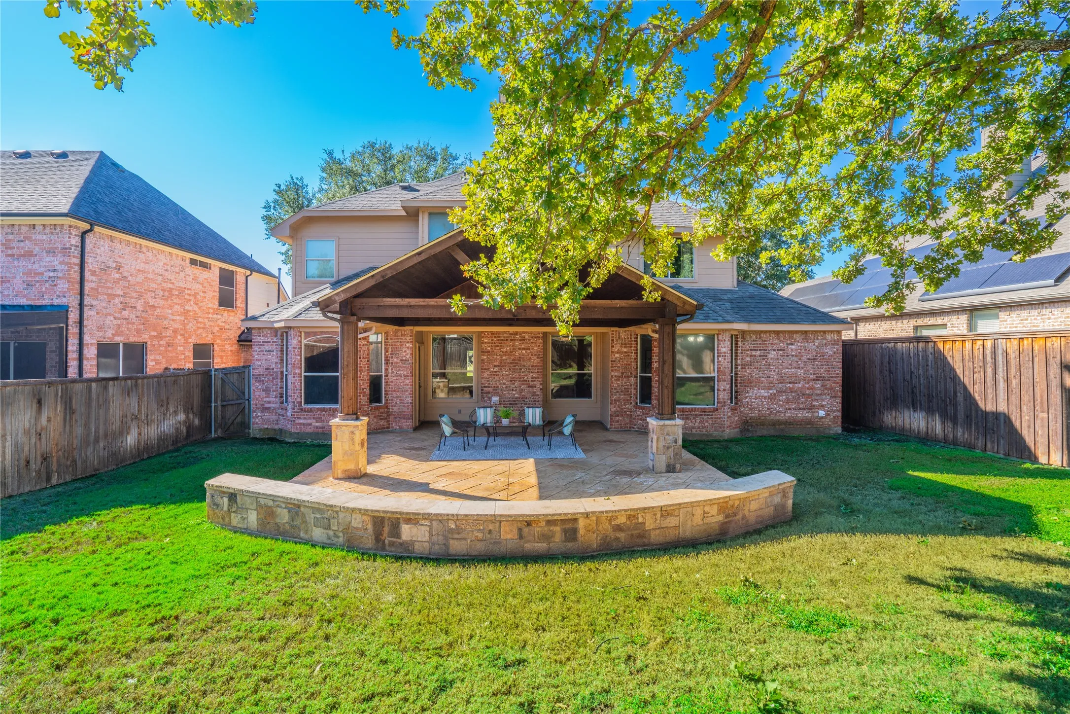 Expansive outdoor living area featuring a covered patio, stone-built retaining wall, and manicured lawn