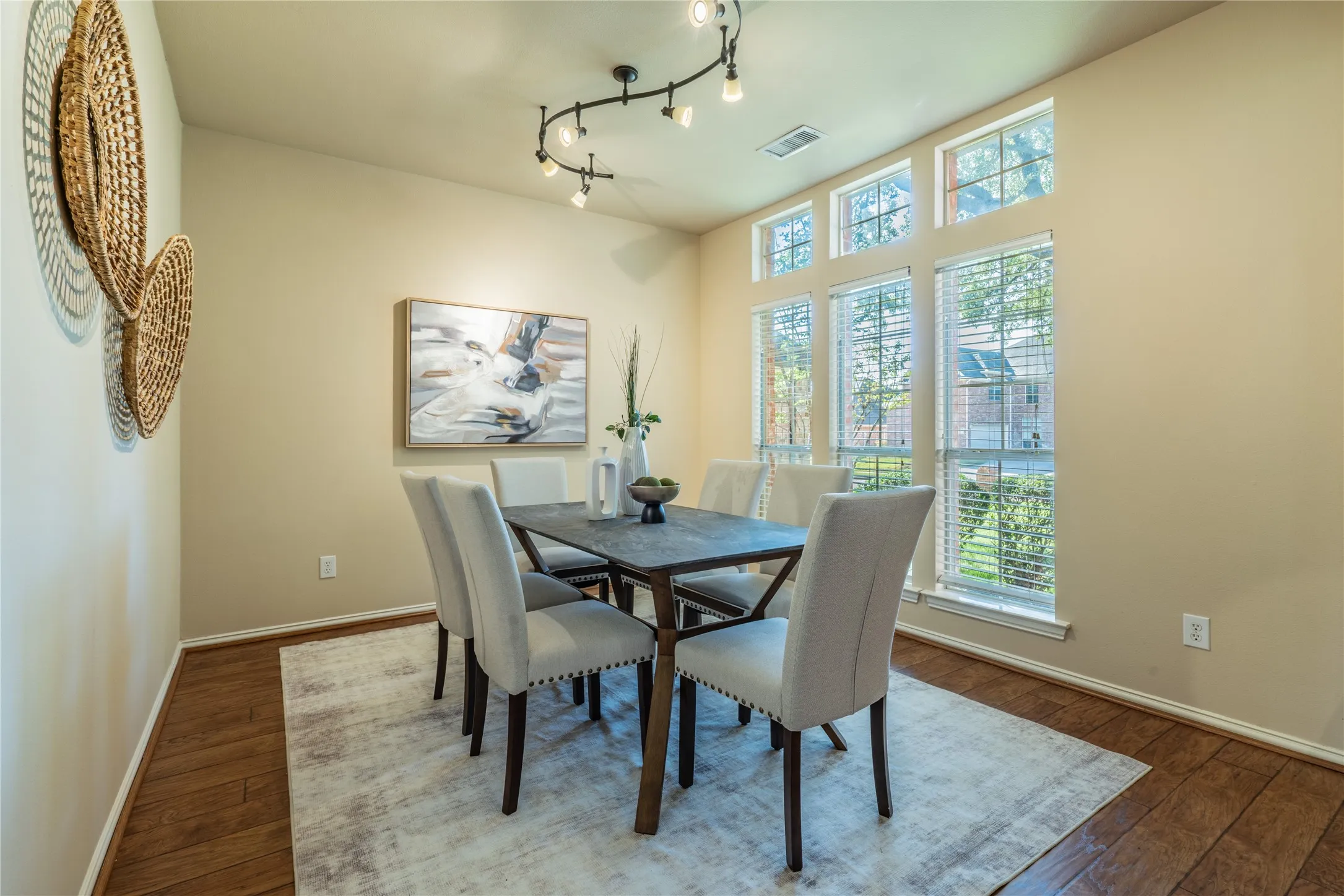 Vaulted ceiling with track lighting, multiple large windows, wood-finish flooring, and neutral wall tones