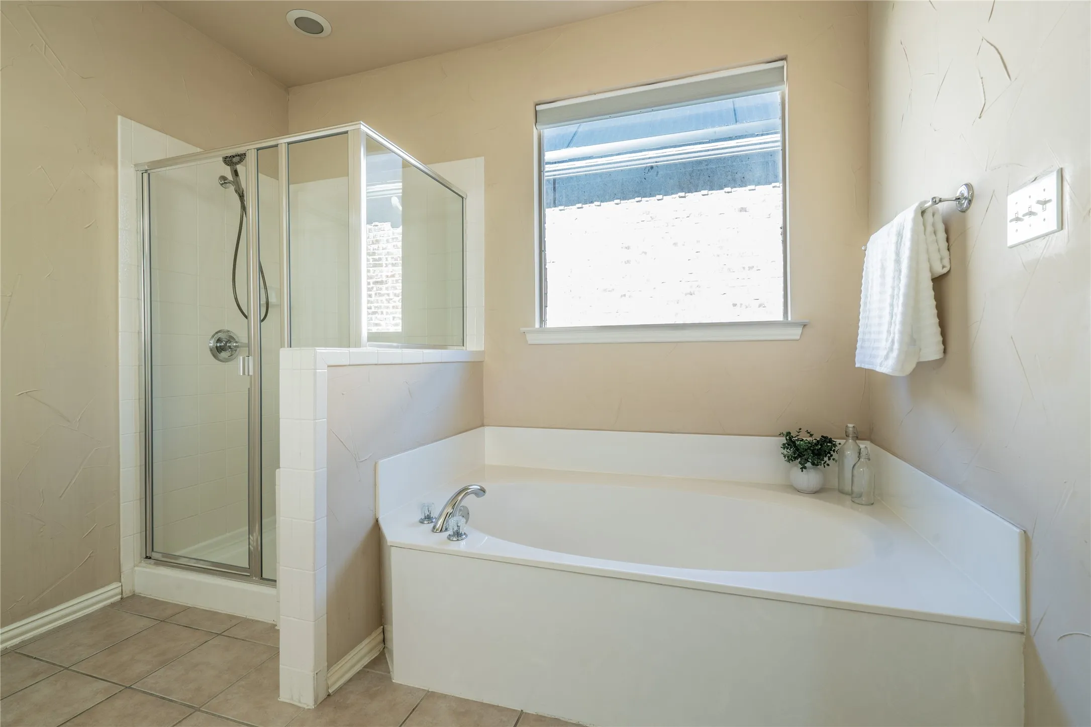 Primary bathoorm with corner soaking tub, glass-enclosed shower, and a large window