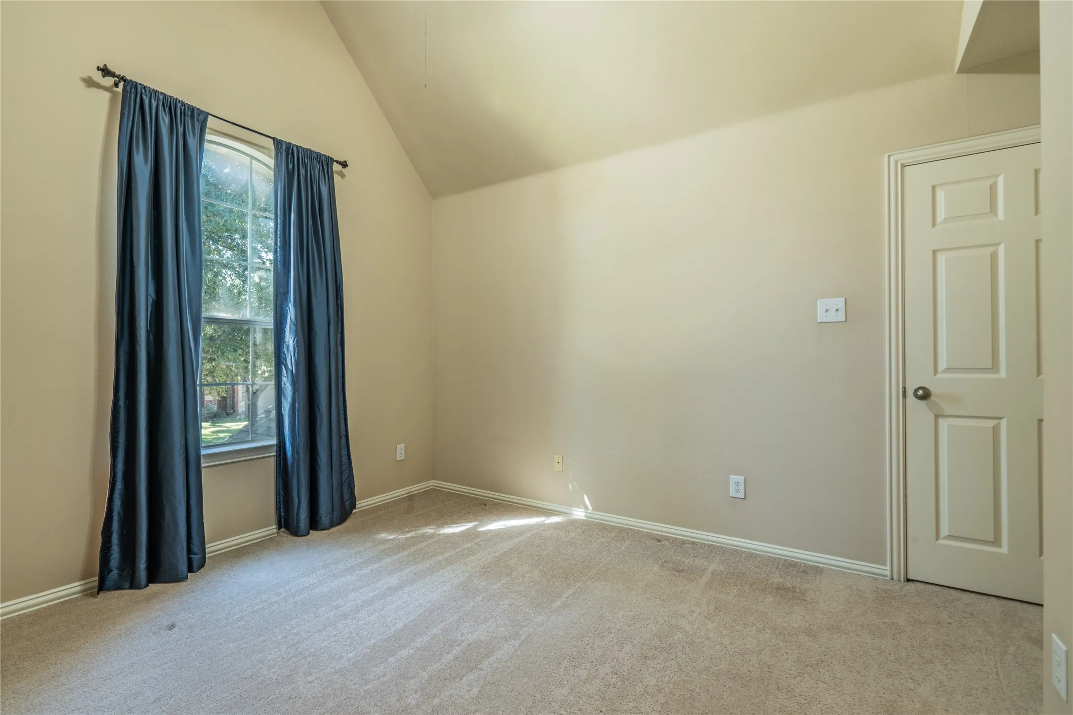 Another view of the bedroom with a vaulted ceiling, carpeted flooring, and a paneled interior door