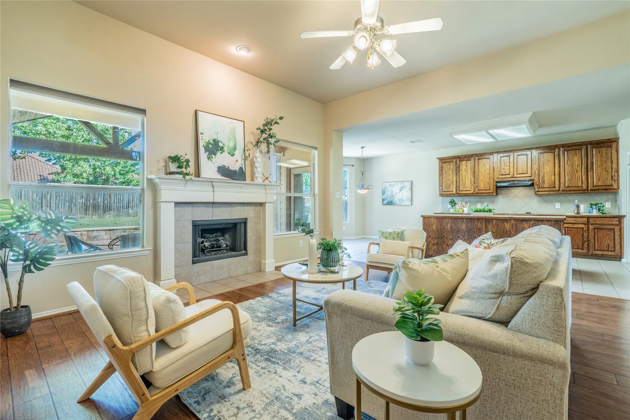 Living area featuring wood-finish flooring, a fireplace with a tiled surround and mantle, a ceiling fan, and large windows