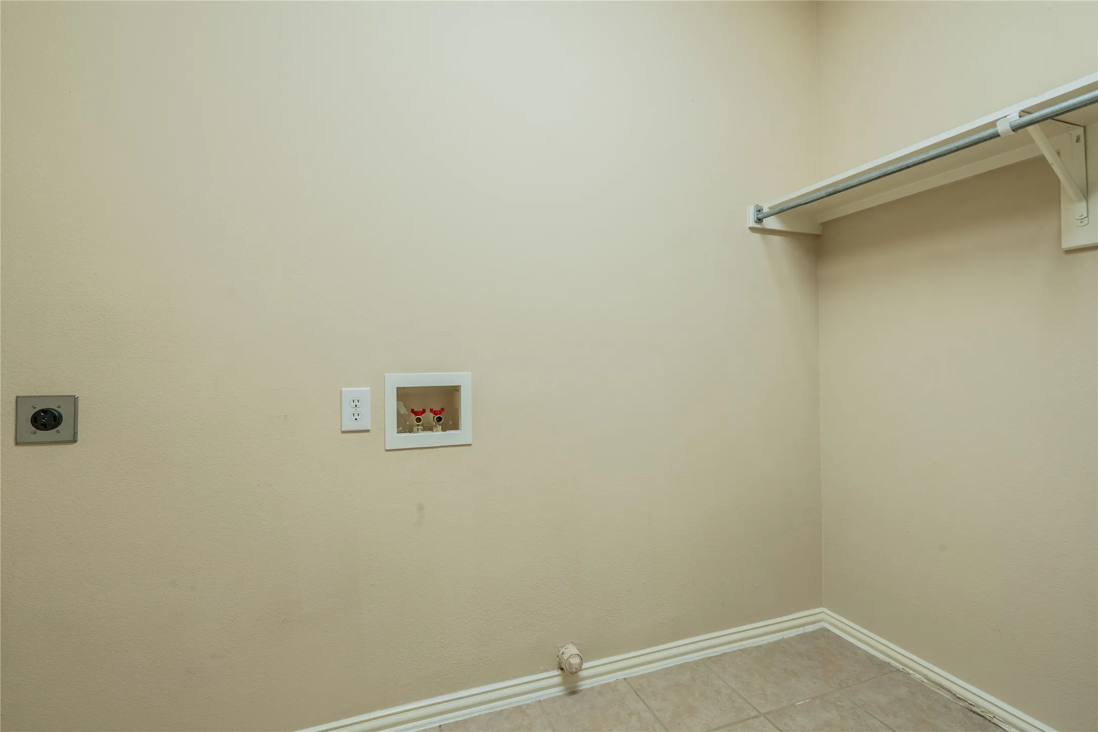 Laundry area with tiled flooring, neutral wall paint, overhead shelving, and integrated utility connections