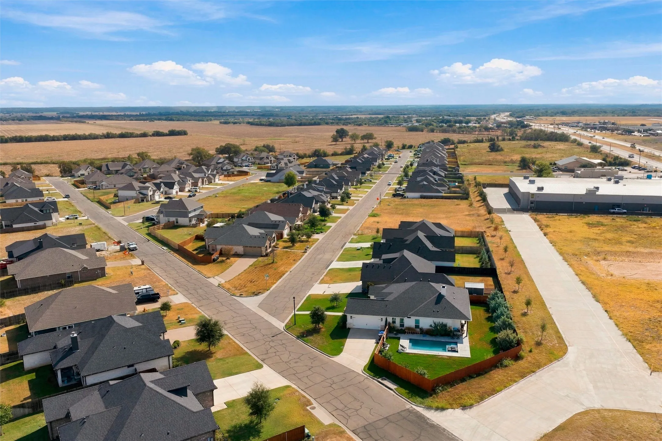 Aerial perspective of a developed residential area with multiple residences, a commercial structure, and roadways, bordered by undeveloped land