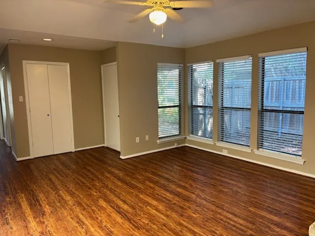 Wood-finish flooring throughout, multiple windows with blinds, ceiling fan with integrated lighting, and guest closet