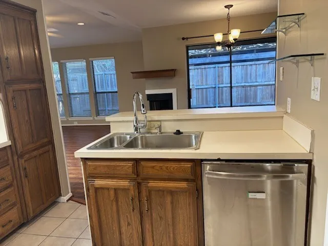 Kitchen featuring wood cabinetry, stainless steel dishwasher, dual basin sink with a gooseneck faucet, light-toned countertops, and tile flooring