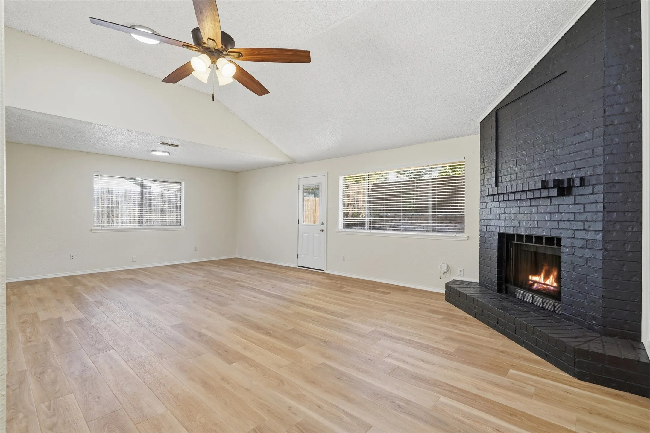 Vaulted ceiling with a ceiling fan, wood-finish flooring, black brick fireplace, and multiple windows