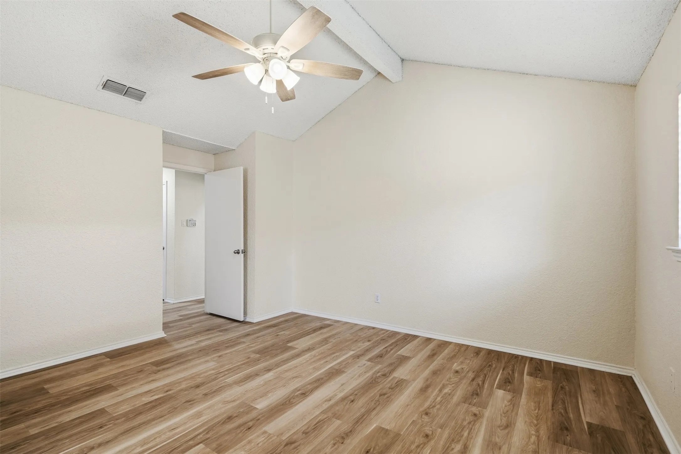 Vaulted ceiling with exposed beam, wood-finish flooring, ceiling fan with integrated lighting, and white trim
