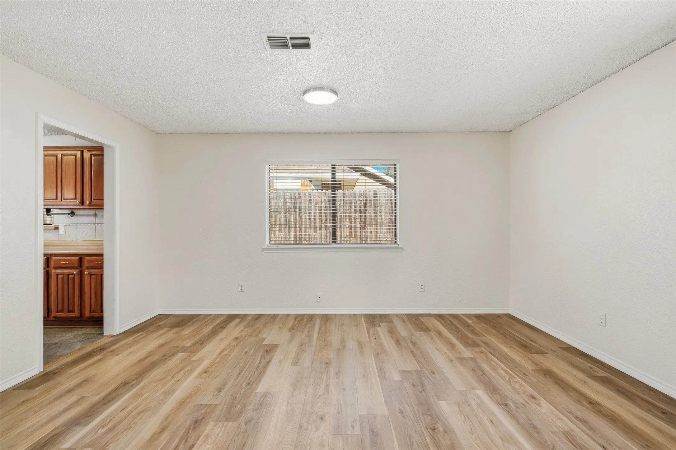 Spacious room featuring wood-finish flooring, a window with blinds, and a flush-mount ceiling light
