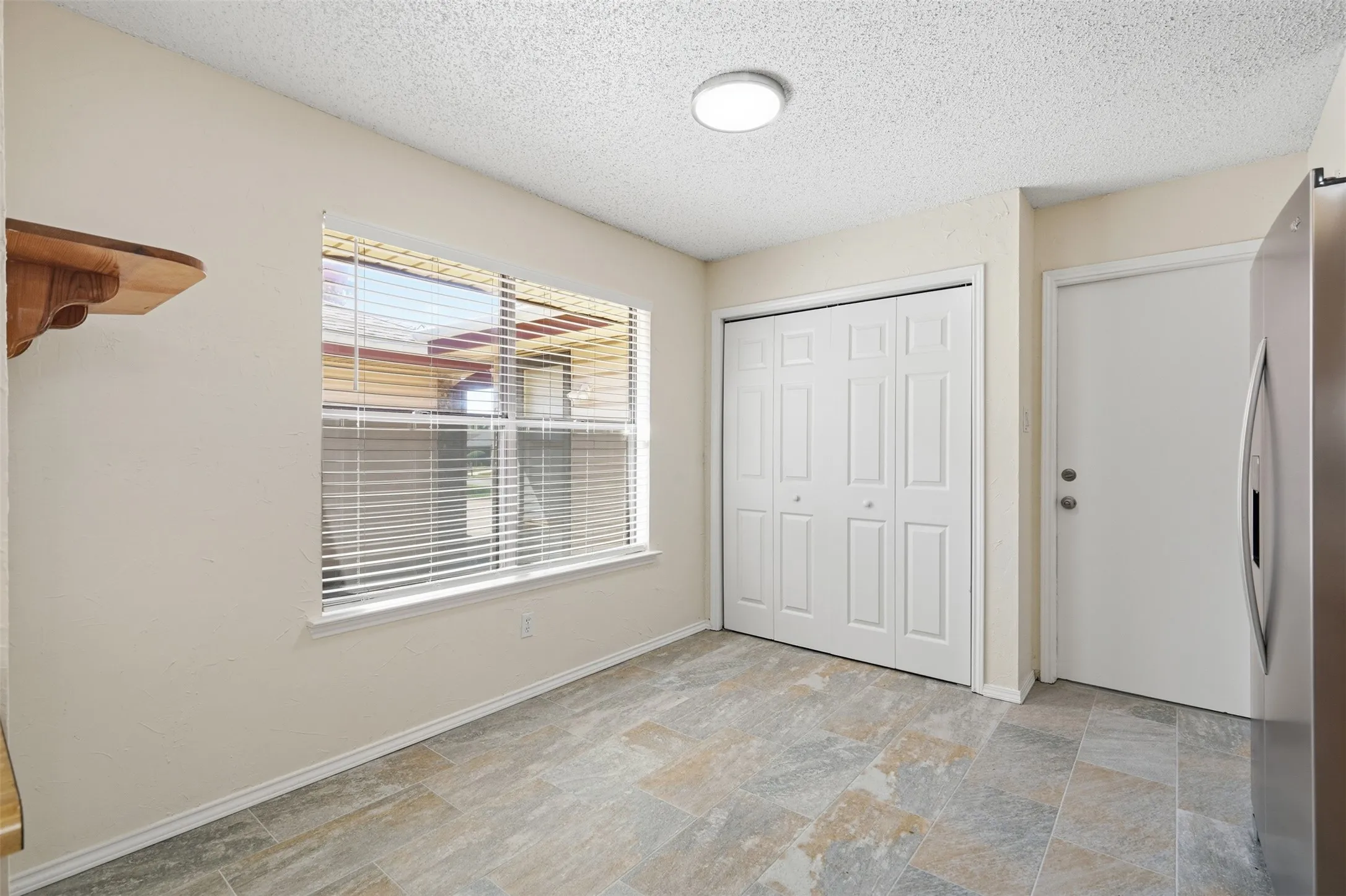 Recessed lighting illuminates the space featuring large window with blinds, tile flooring, and white bifold closet doors