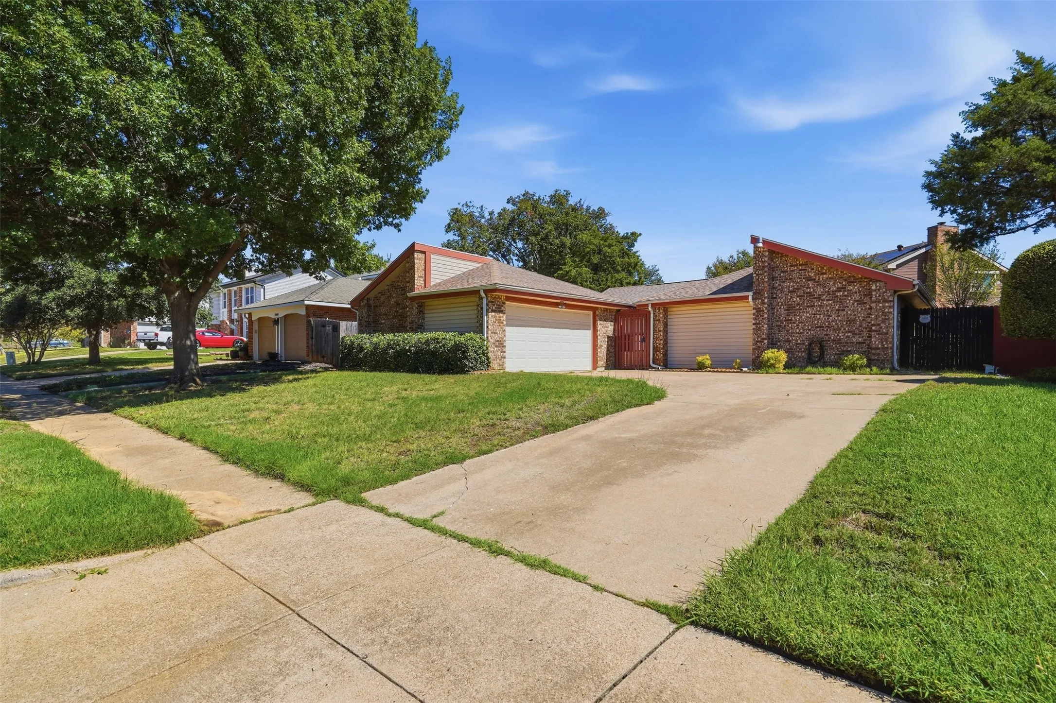 Brick and siding exterior with a multi-car driveway, attached garages, and mature trees