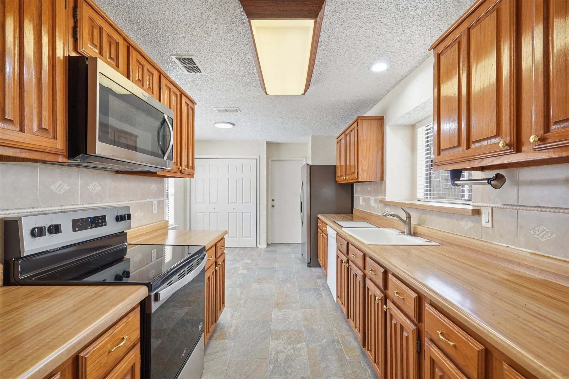 Galley kitchen with wood cabinetry, wood-finish countertops, stainless steel appliances, and tile flooring