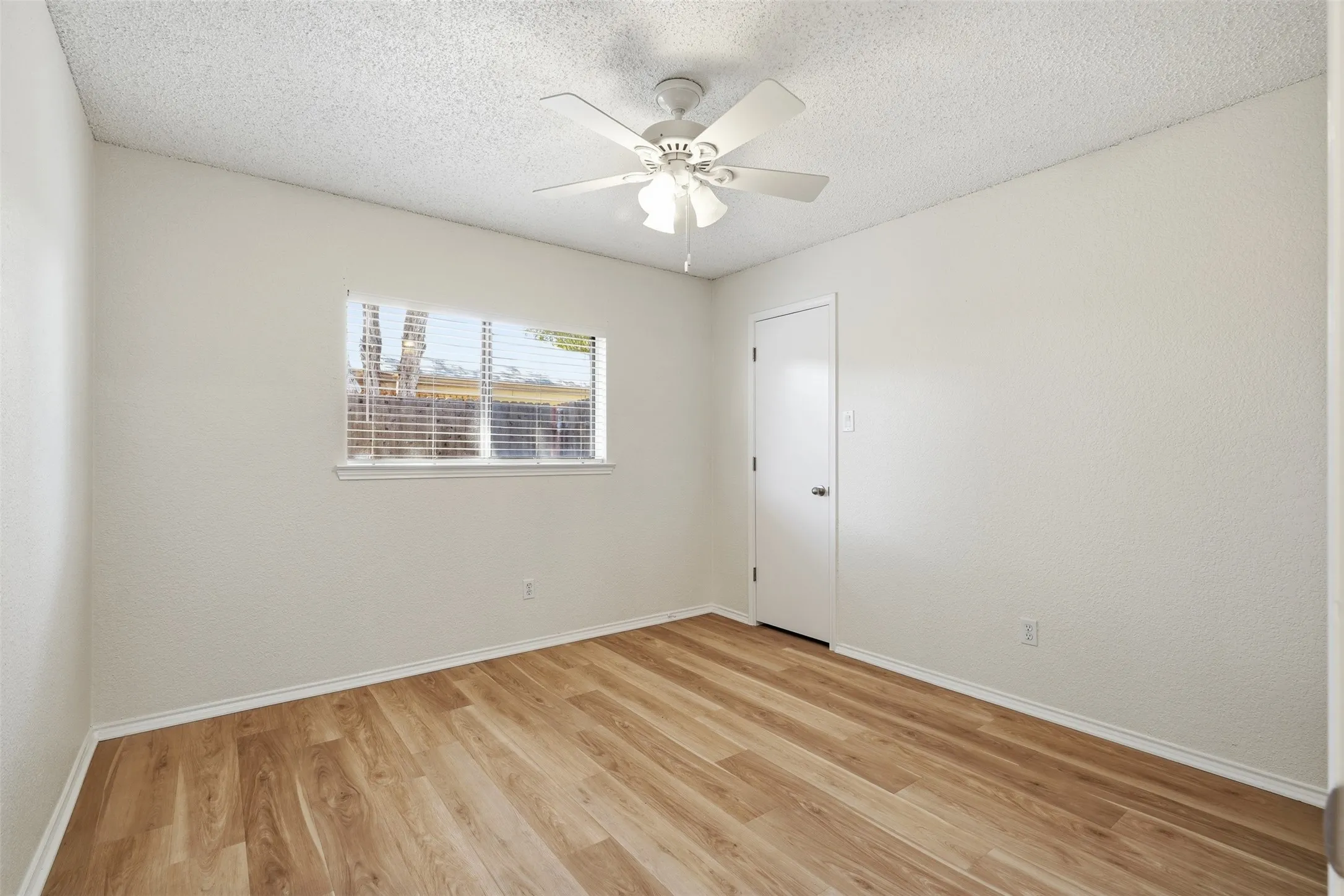 Wood-finish flooring with white trim, a ceiling fan with light fixture, and window with blinds