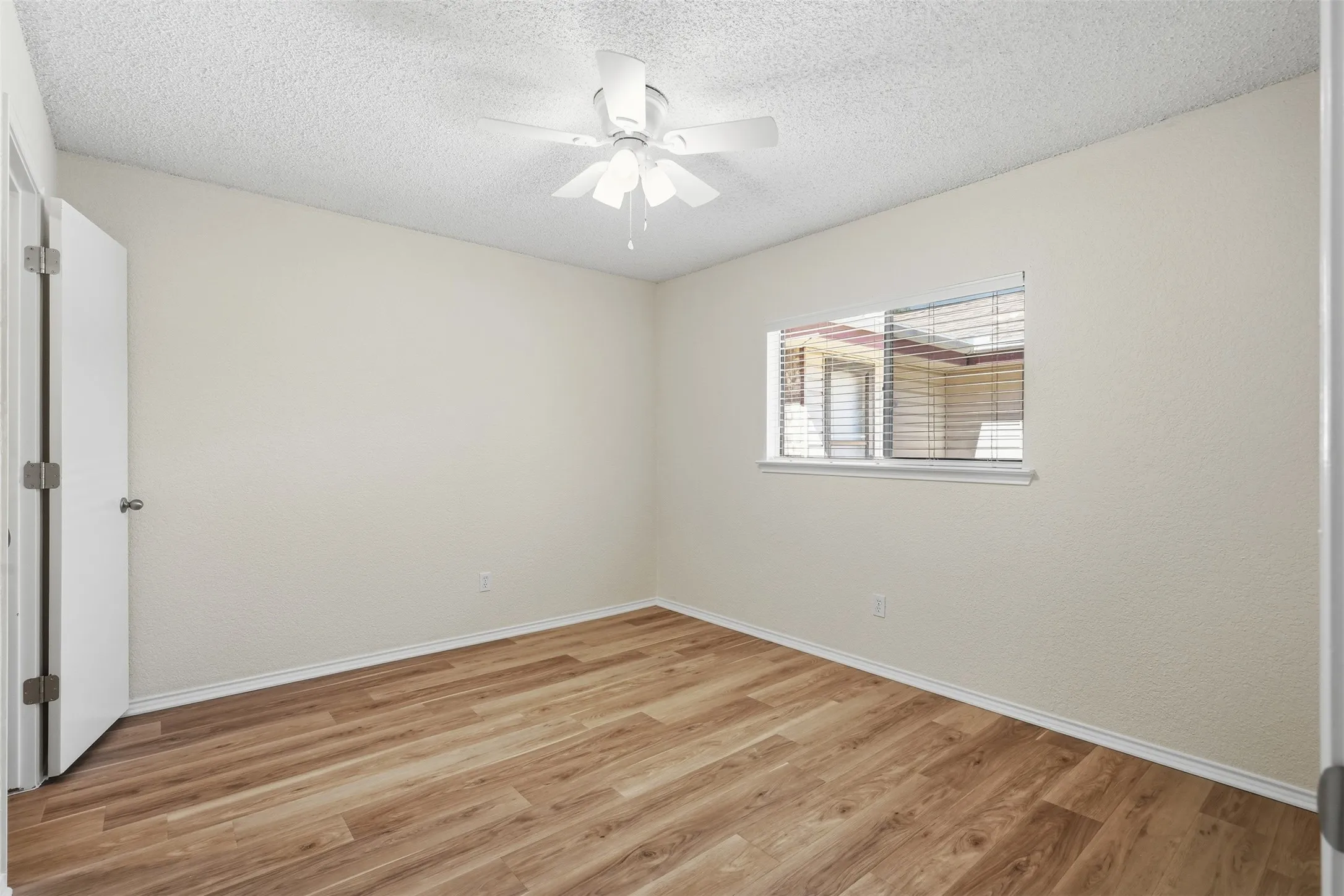 Light wood-finish flooring, textured wall finishes, and a single window with blinds