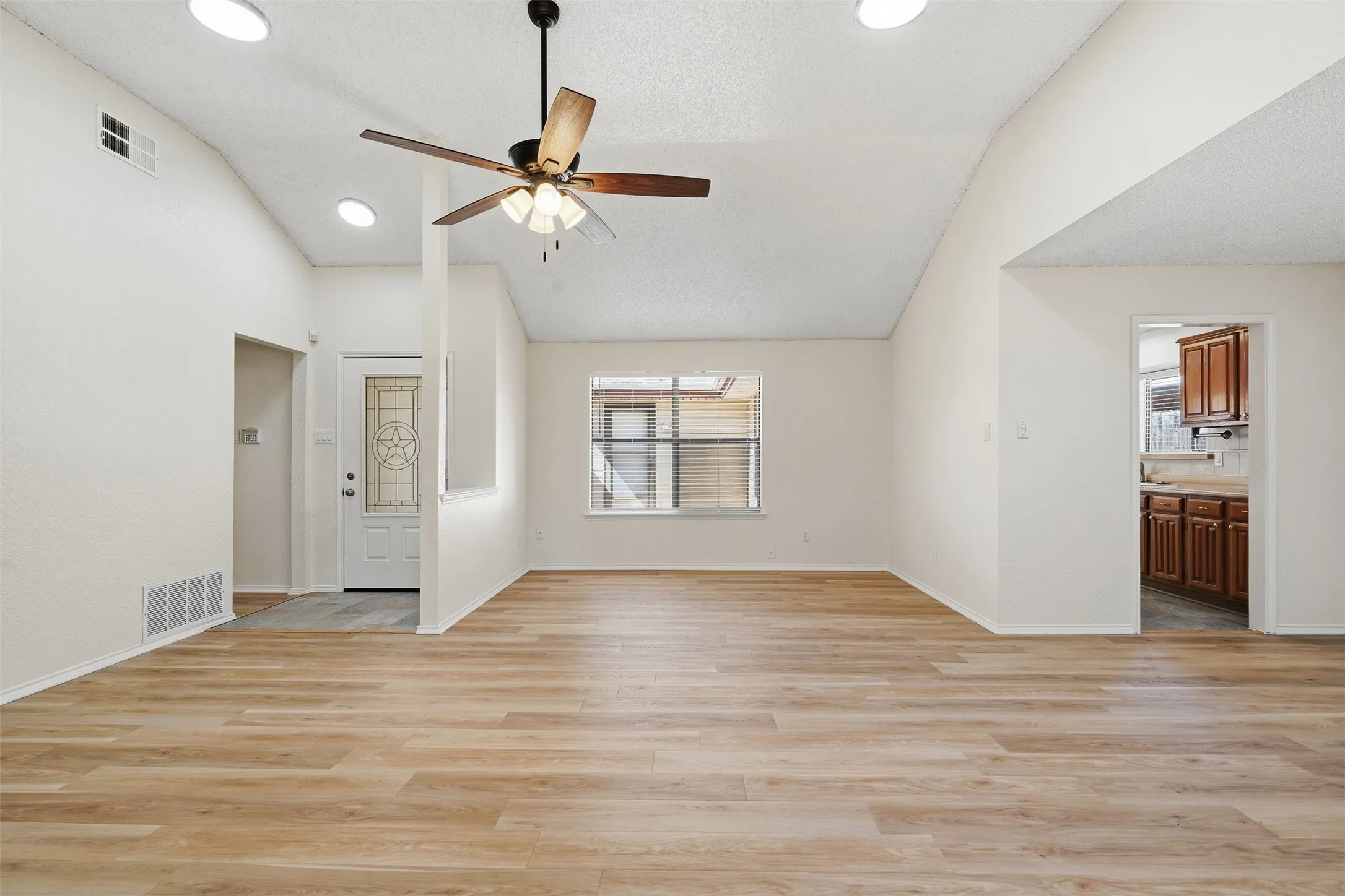 Vaulted ceilings with recessed lighting, wood-finish flooring, a decorative glass entry door, and a ceiling fan with integrated lighting