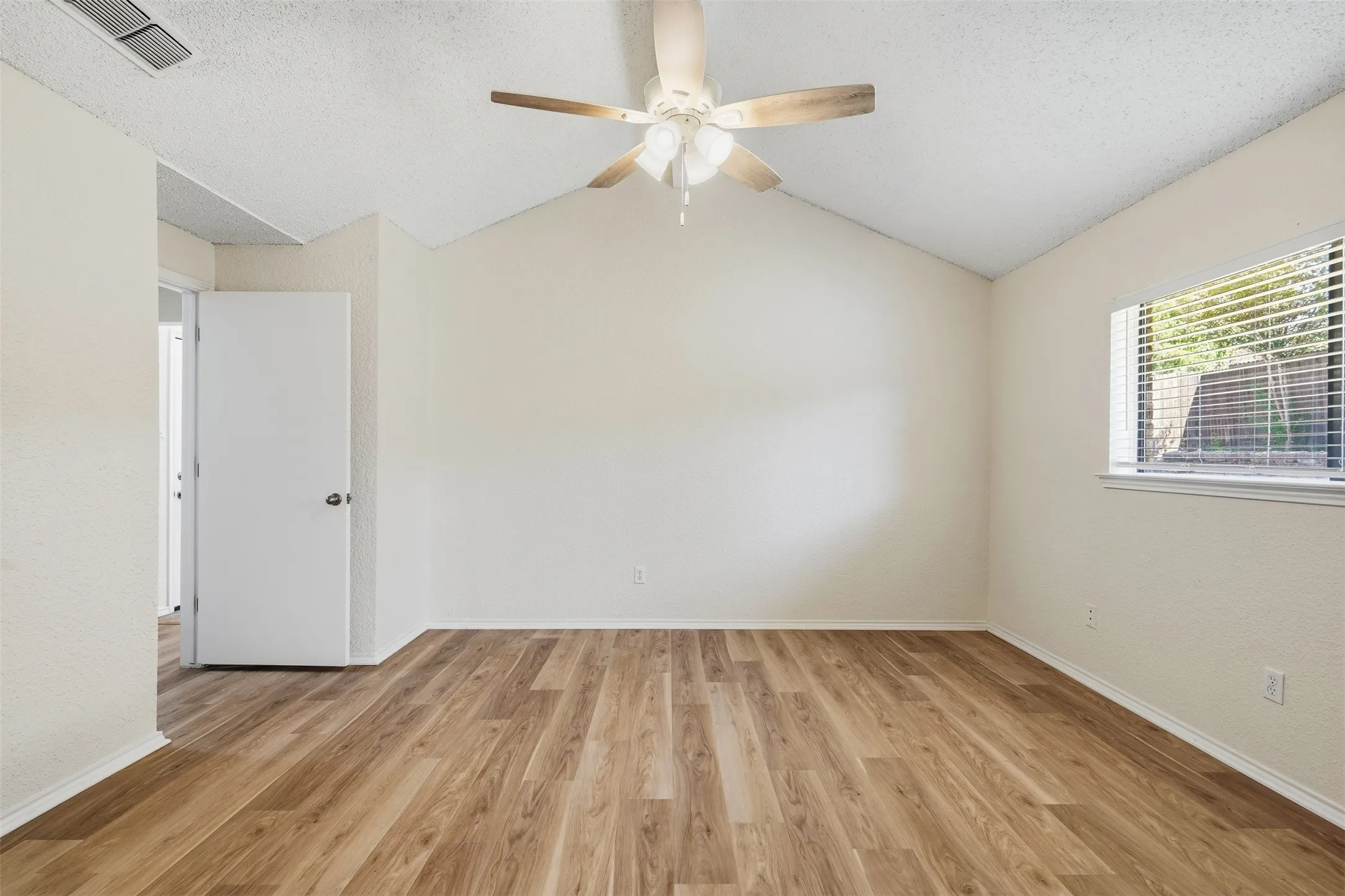 Vaulted ceiling with a ceiling fan, wood-finish flooring, and a window with blinds
