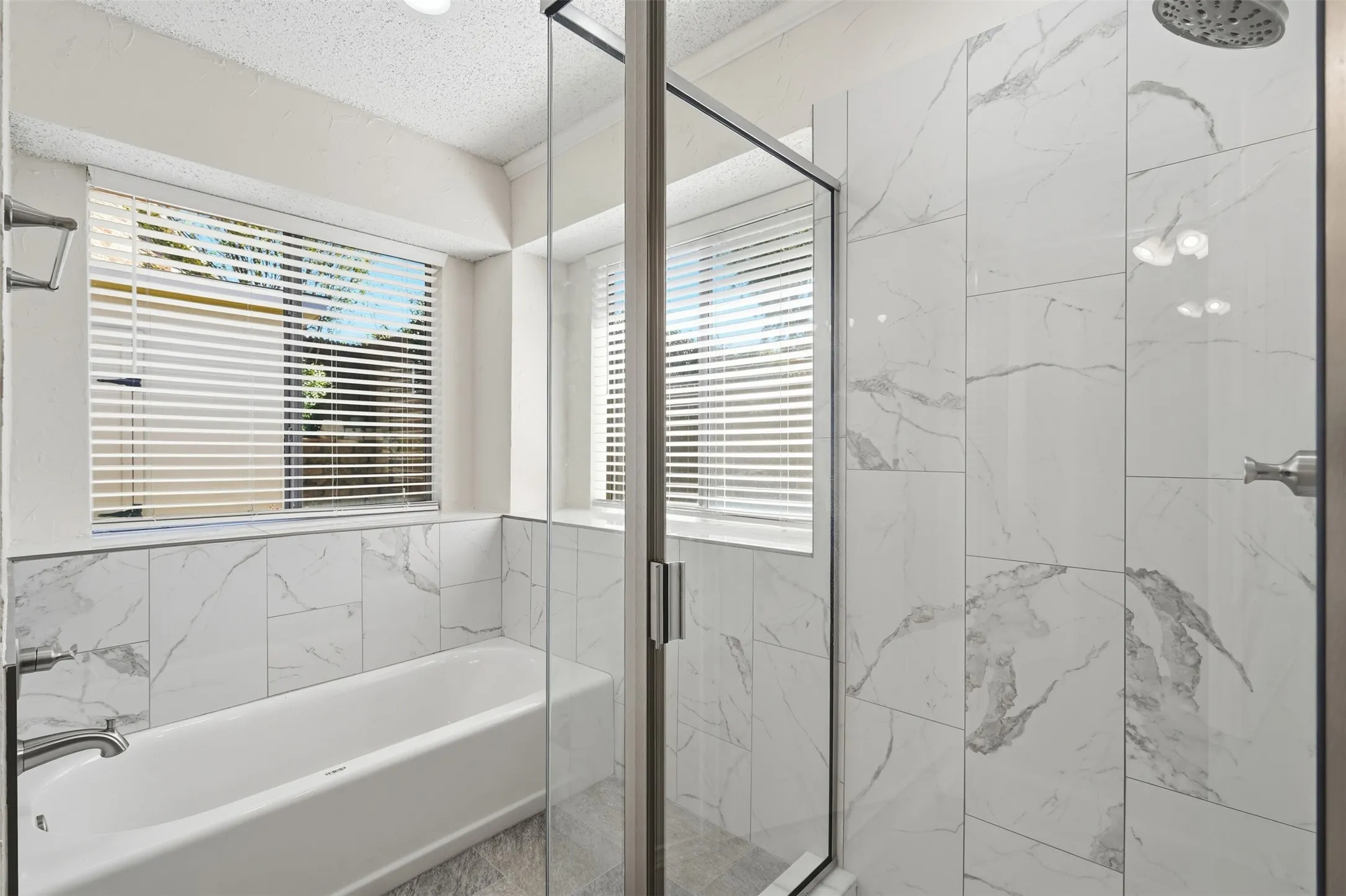 Bathtub with white subway tile surround, clear glass shower enclosure, rain showerhead, and window with horizontal blinds