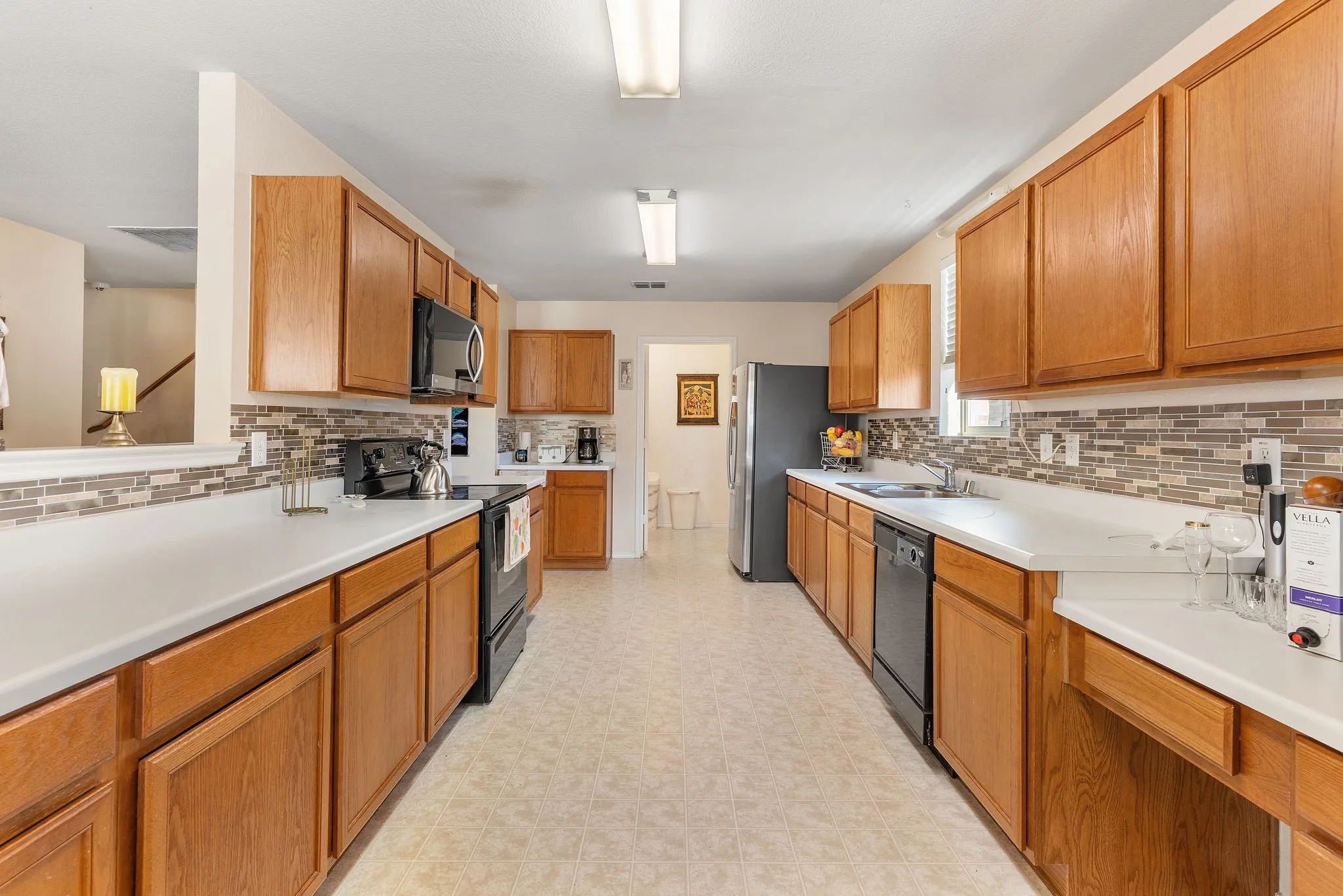 Galley kitchen featuring wood cabinetry, solid surface countertops, mosaic tile backsplash, and built-in appliances