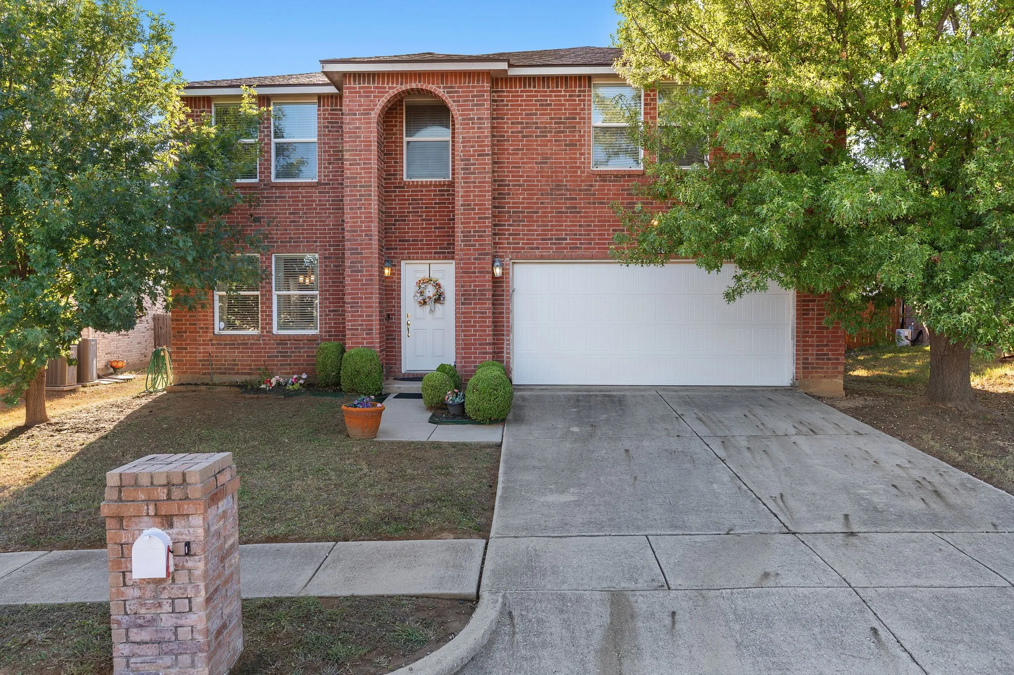 Brick exterior with an arched entryway, attached garage, and concrete driveway