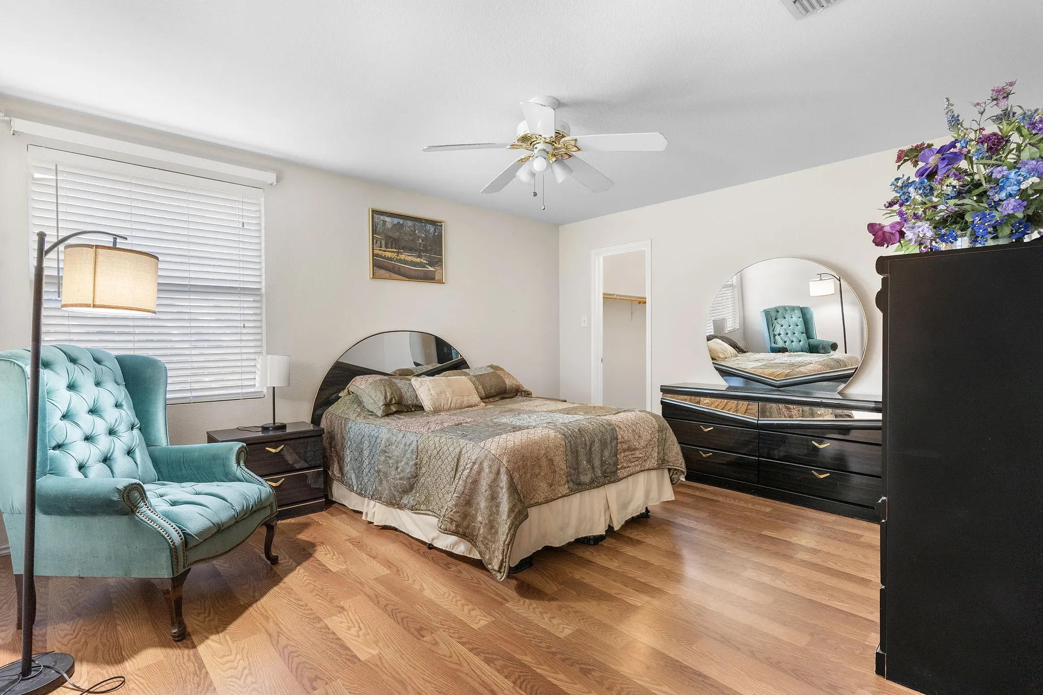 Wood-finish flooring throughout, ceiling fan with light fixture, window with horizontal blinds, and a built-in closet with shelving