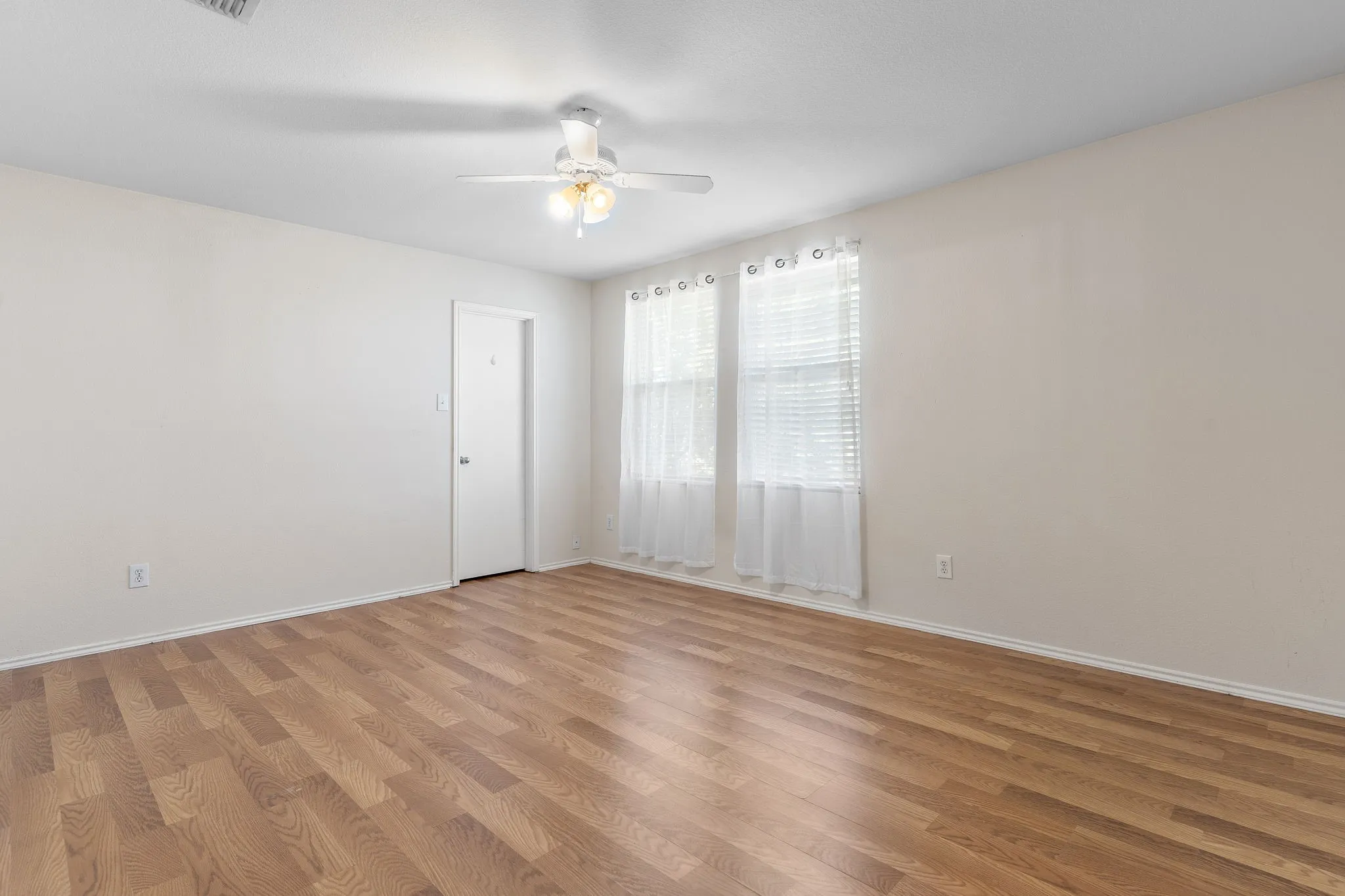 Wood-finish flooring throughout, white walls, and a ceiling fan with integrated lighting